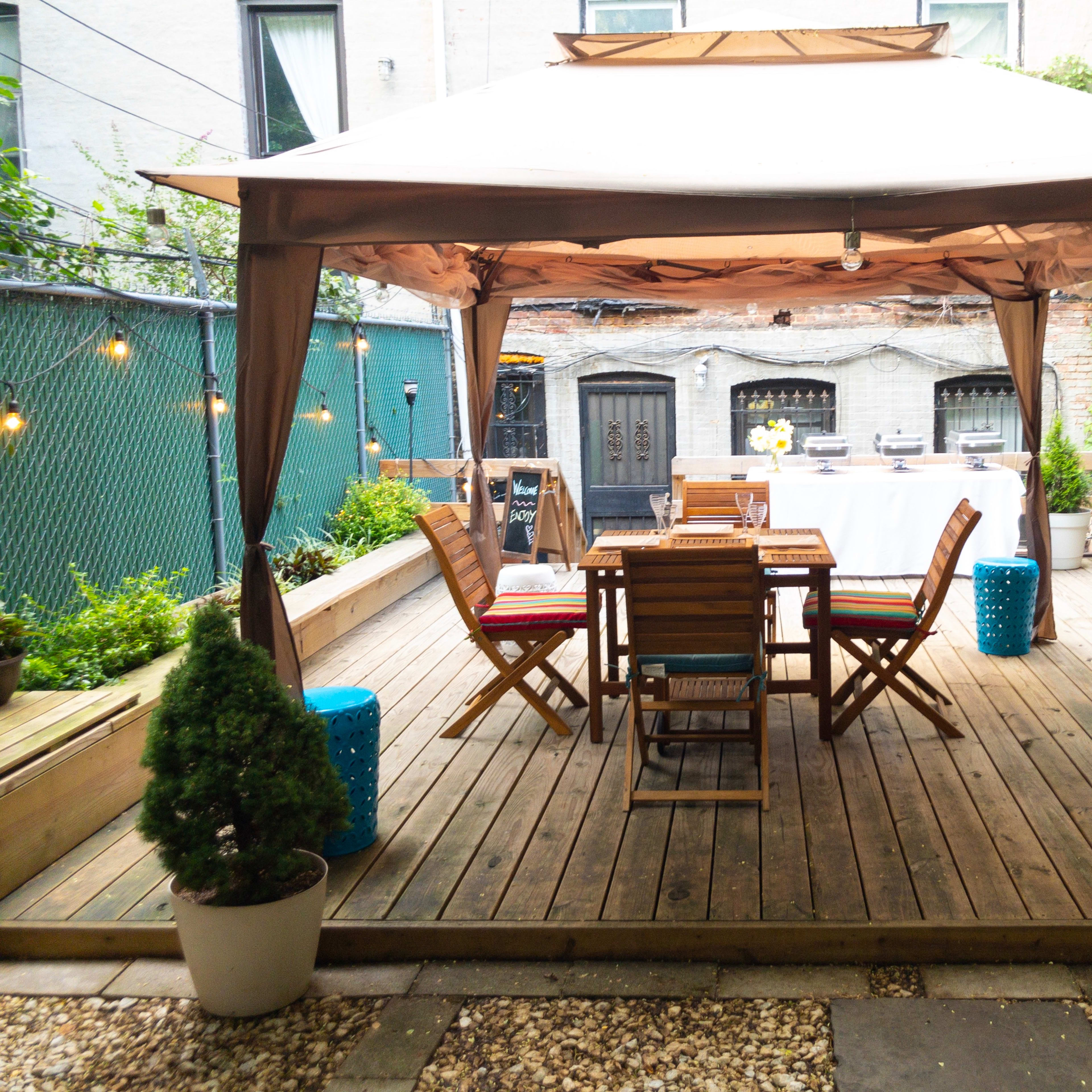 A wooden deck features a gazebo with a dining table and chairs surrounded by plants and decorative elements.