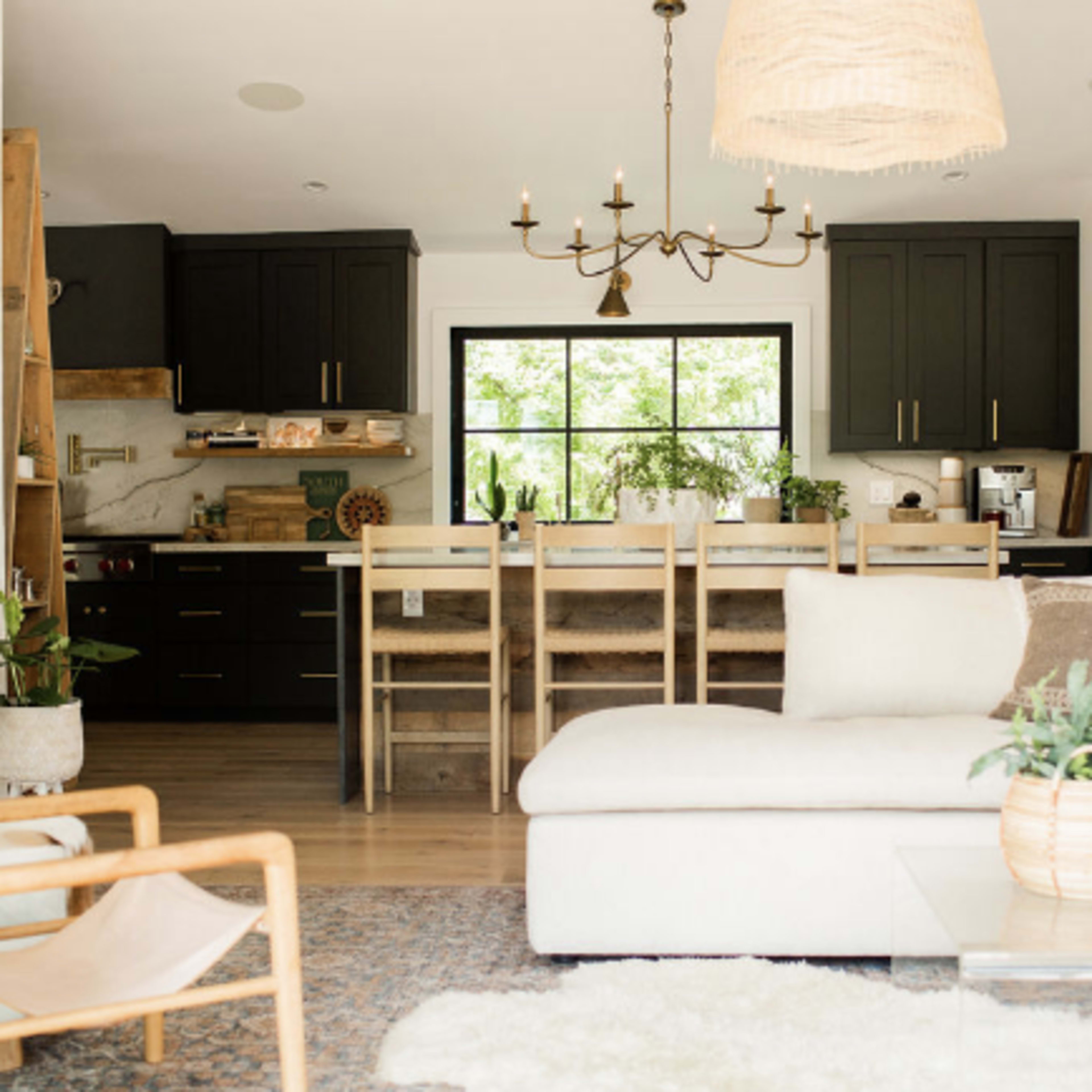 A modern kitchen and living area with black cabinetry, a large window, and a sectional sofa arranged around a glass coffee table.
