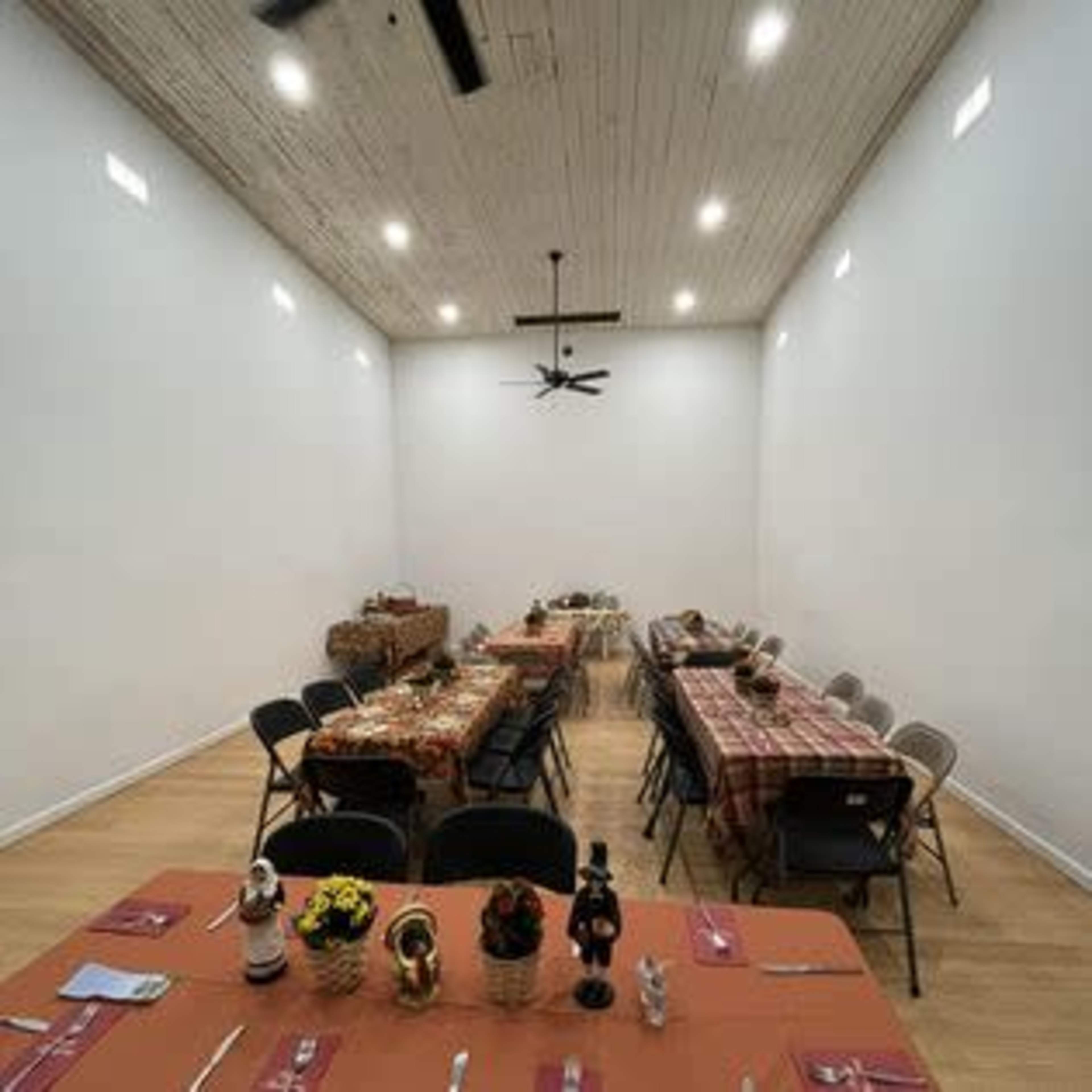 A dining room features several tables set with place settings and decorated with tablecloths, arranged in a way that accommodates multiple guests.