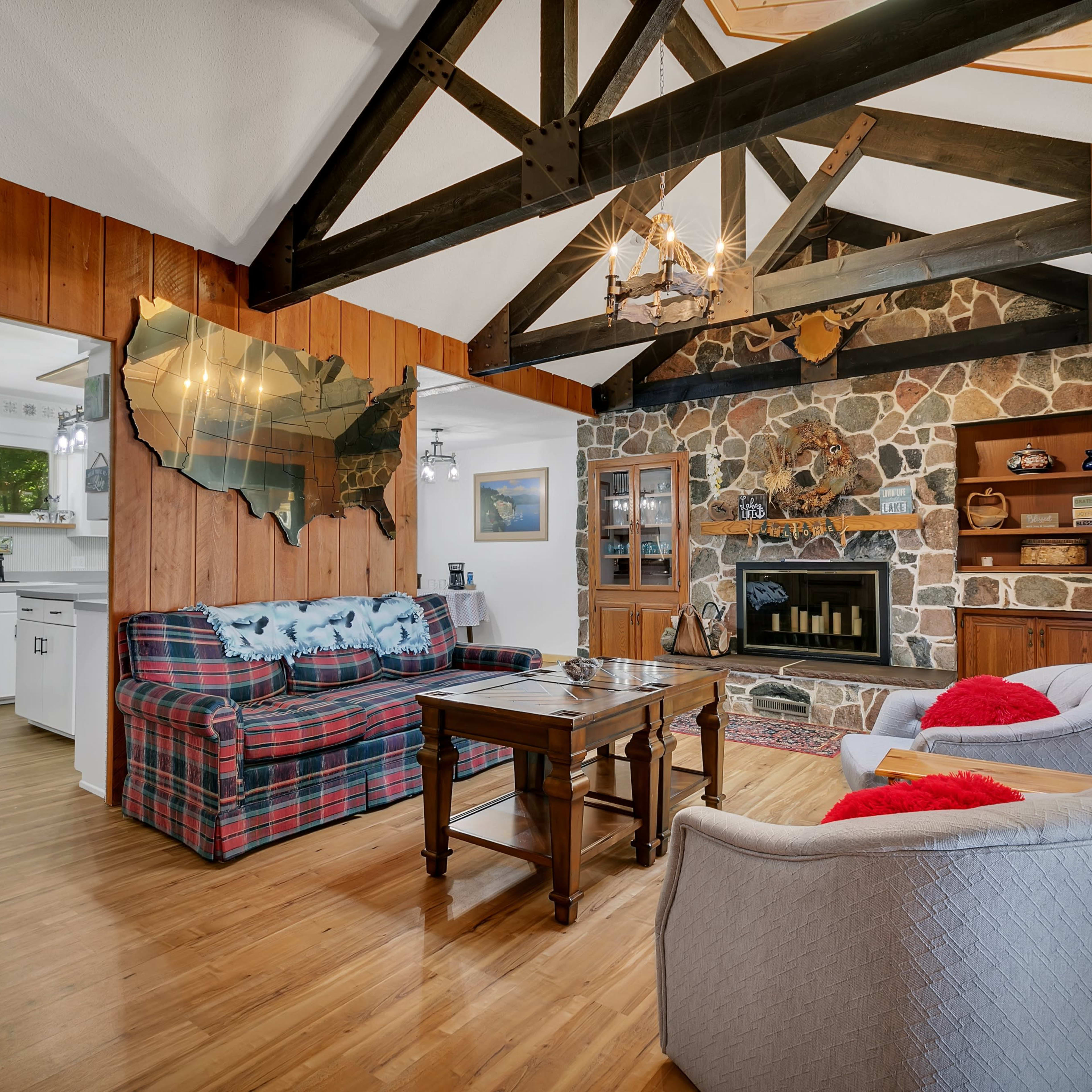 The living room features a stone fireplace, wooden beams, and a plaid sofa with a wooden coffee table.