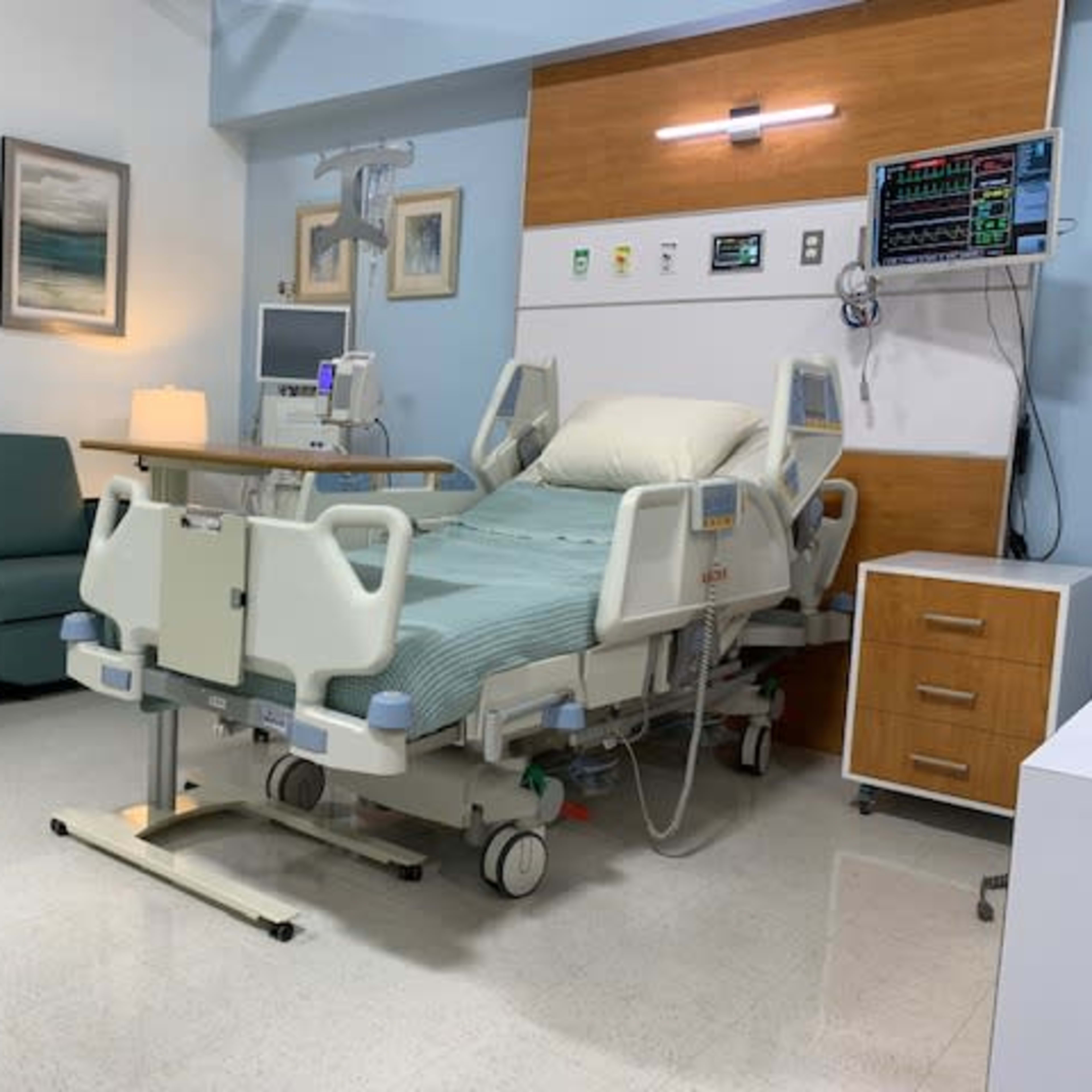 A hospital room with a bed, a couch, a nightstand, and medical equipment on the wall.