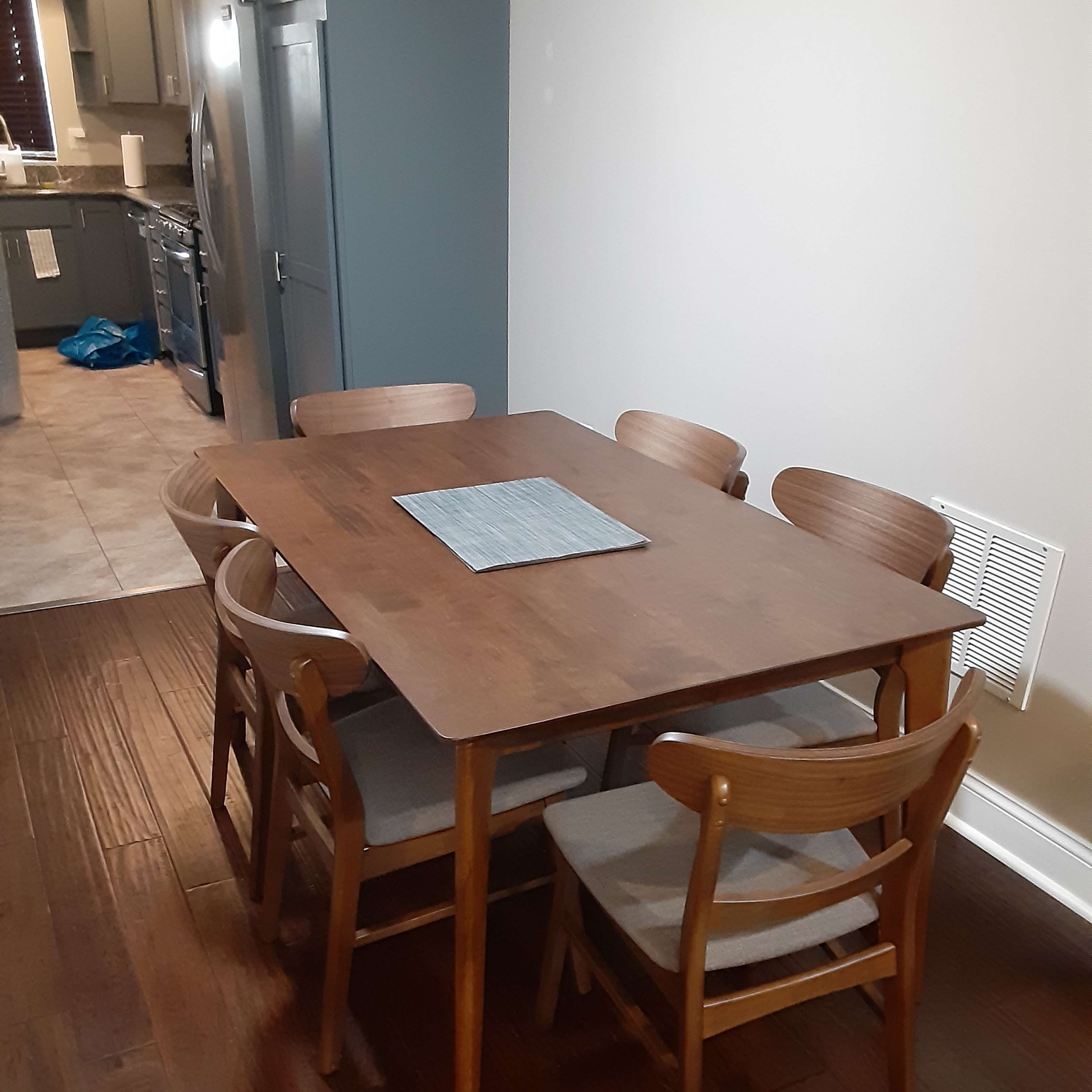A wooden dining table with six chairs is set in a kitchen area, next to cabinets and appliances.