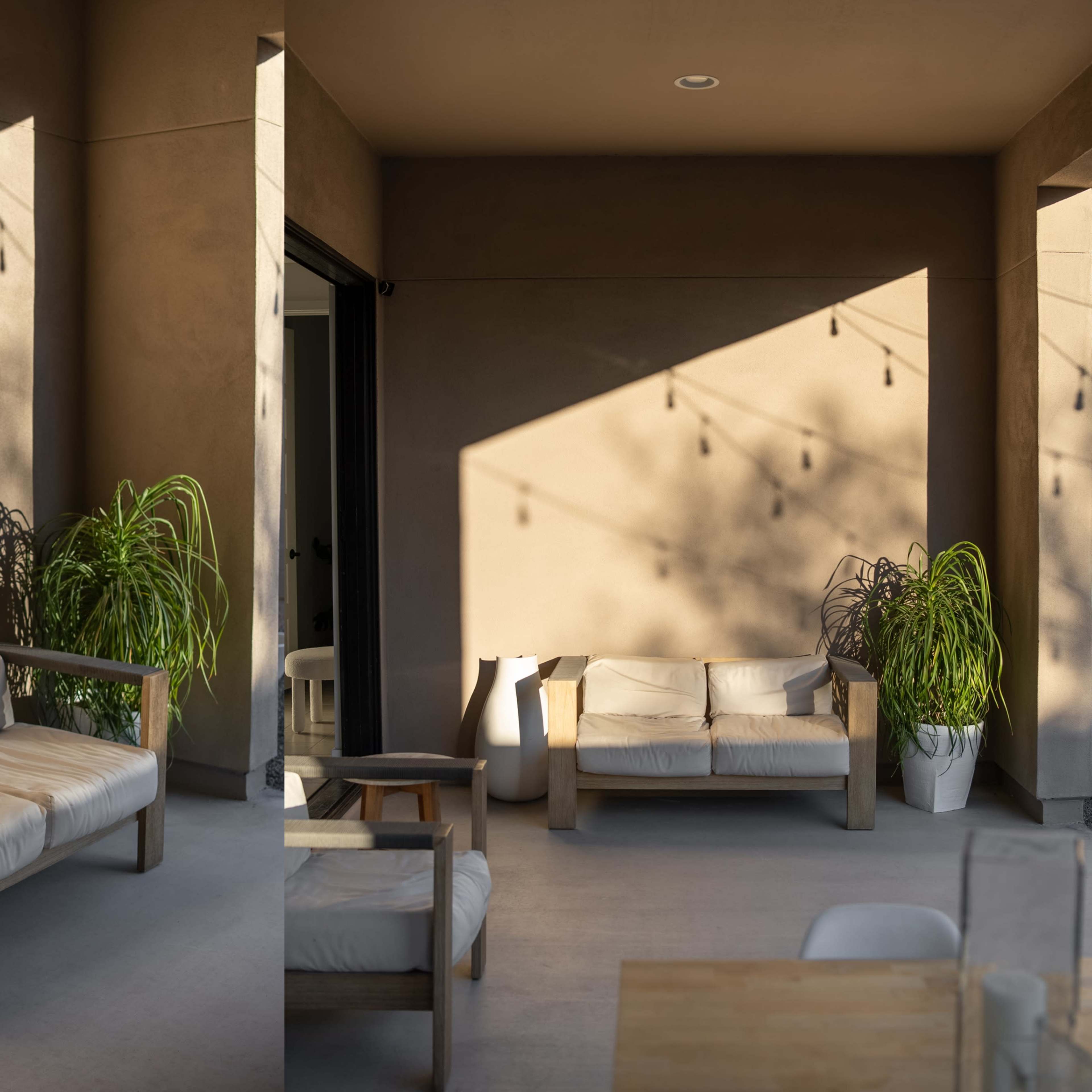 A modern, minimalist outdoor seating area with a white couch and a potted plant, illuminated by soft shadows against a textured wall.