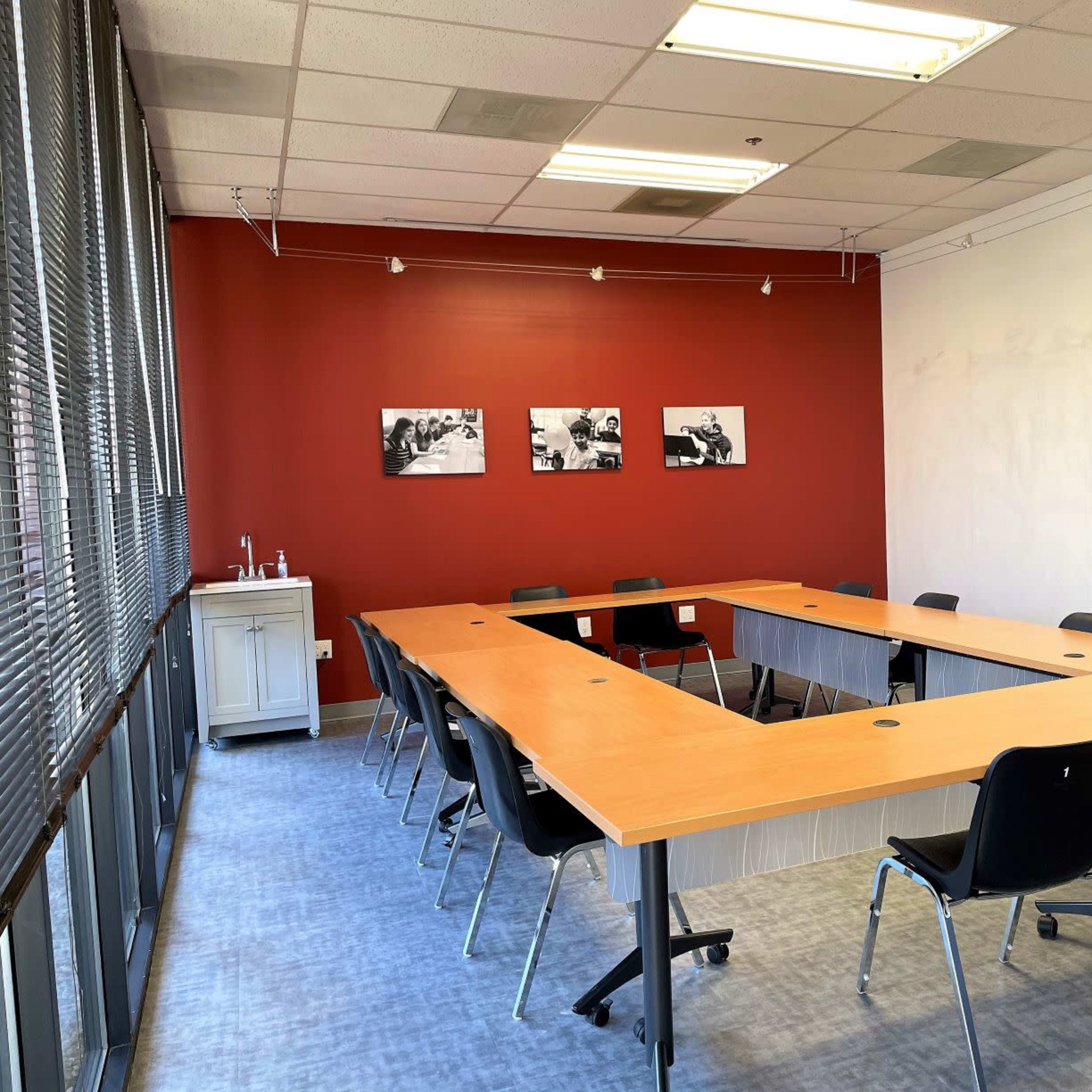 A conference room featuring a rectangular table surrounded by black chairs, with a red accent wall displaying three black-and-white photographs.