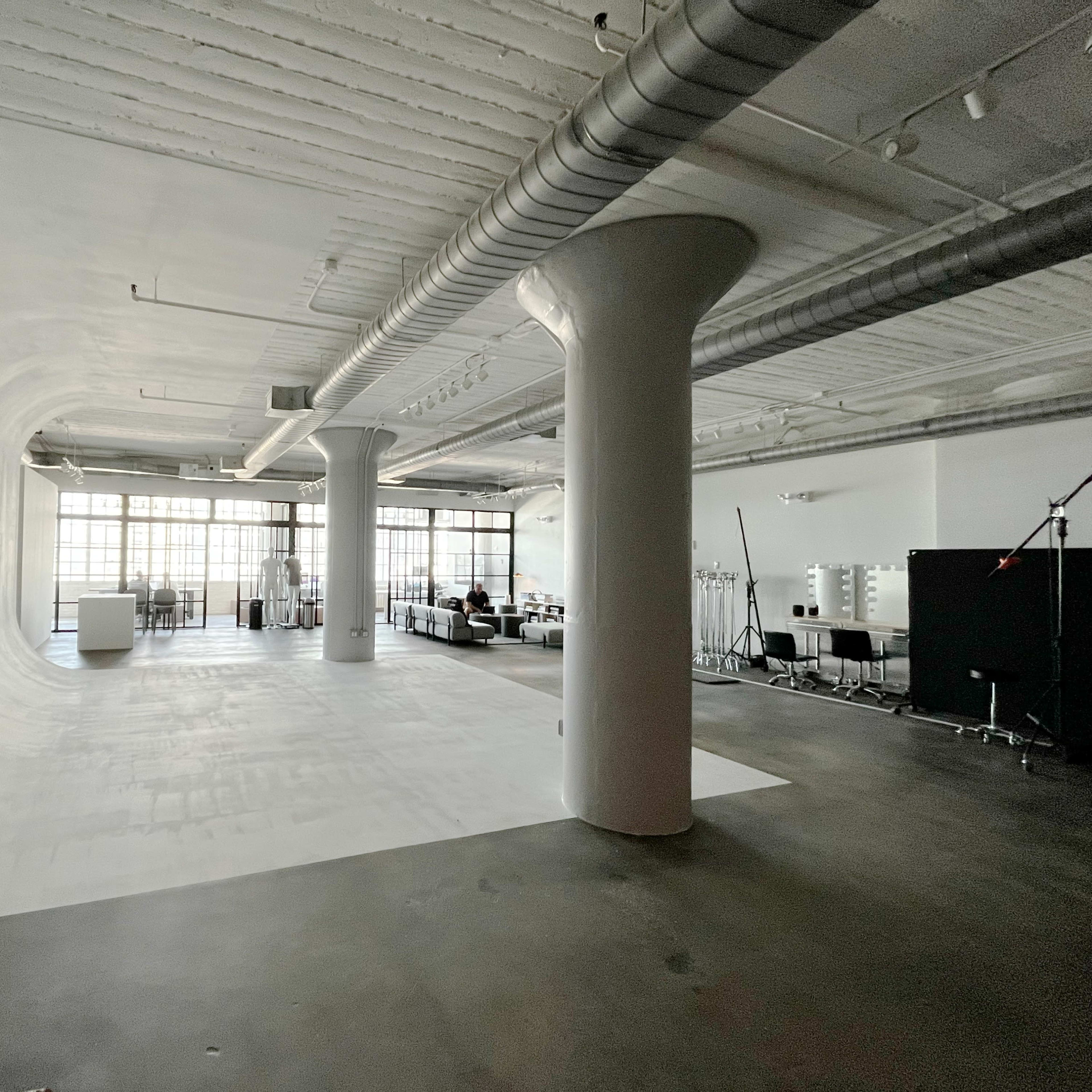 A spacious studio with a white, curved backdrop, large windows letting in natural light, and minimal furnishings.
