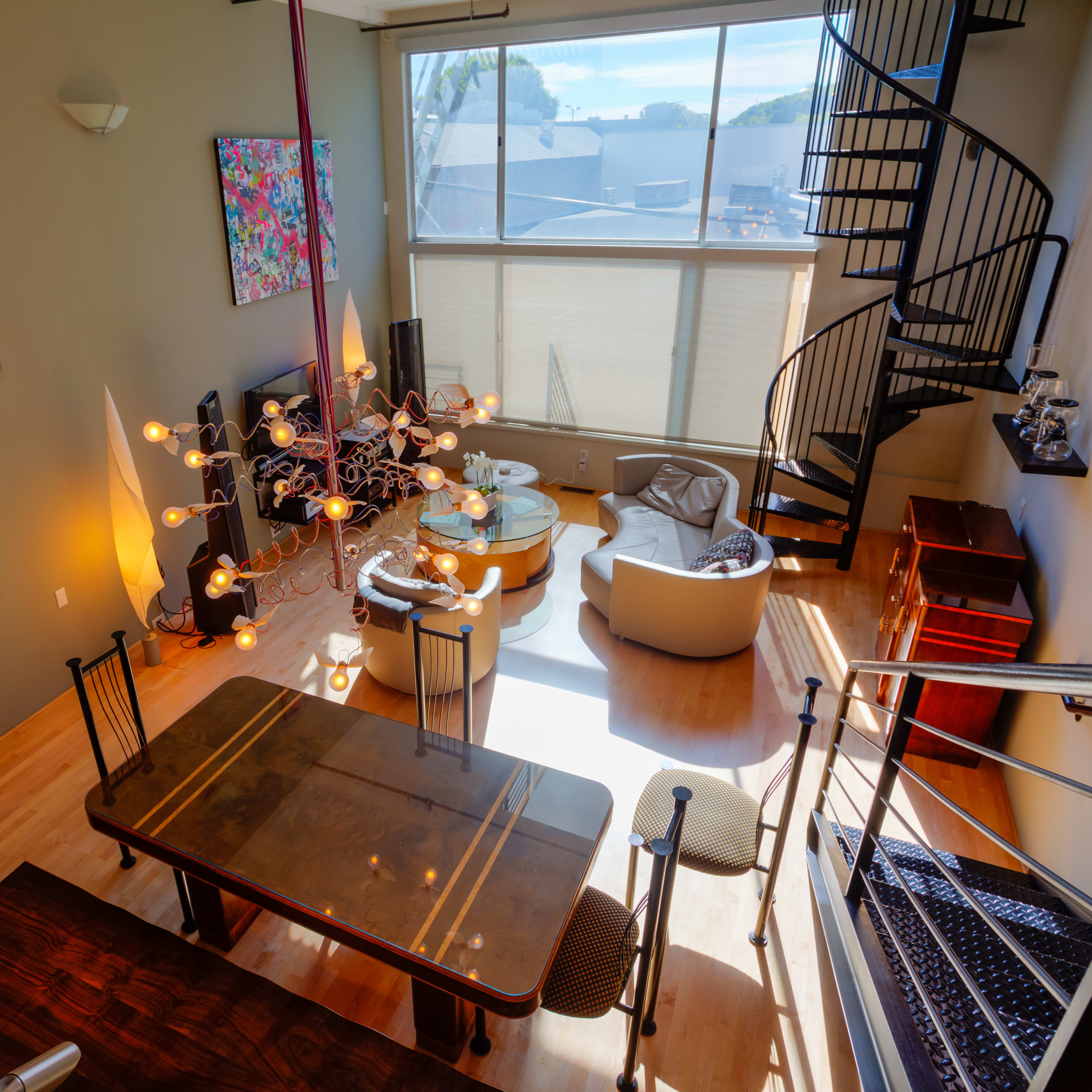 A modern, multi-level living space features a dining area with a wooden table, a lounge with a circular sofa, and a spiral staircase leading to a loft.