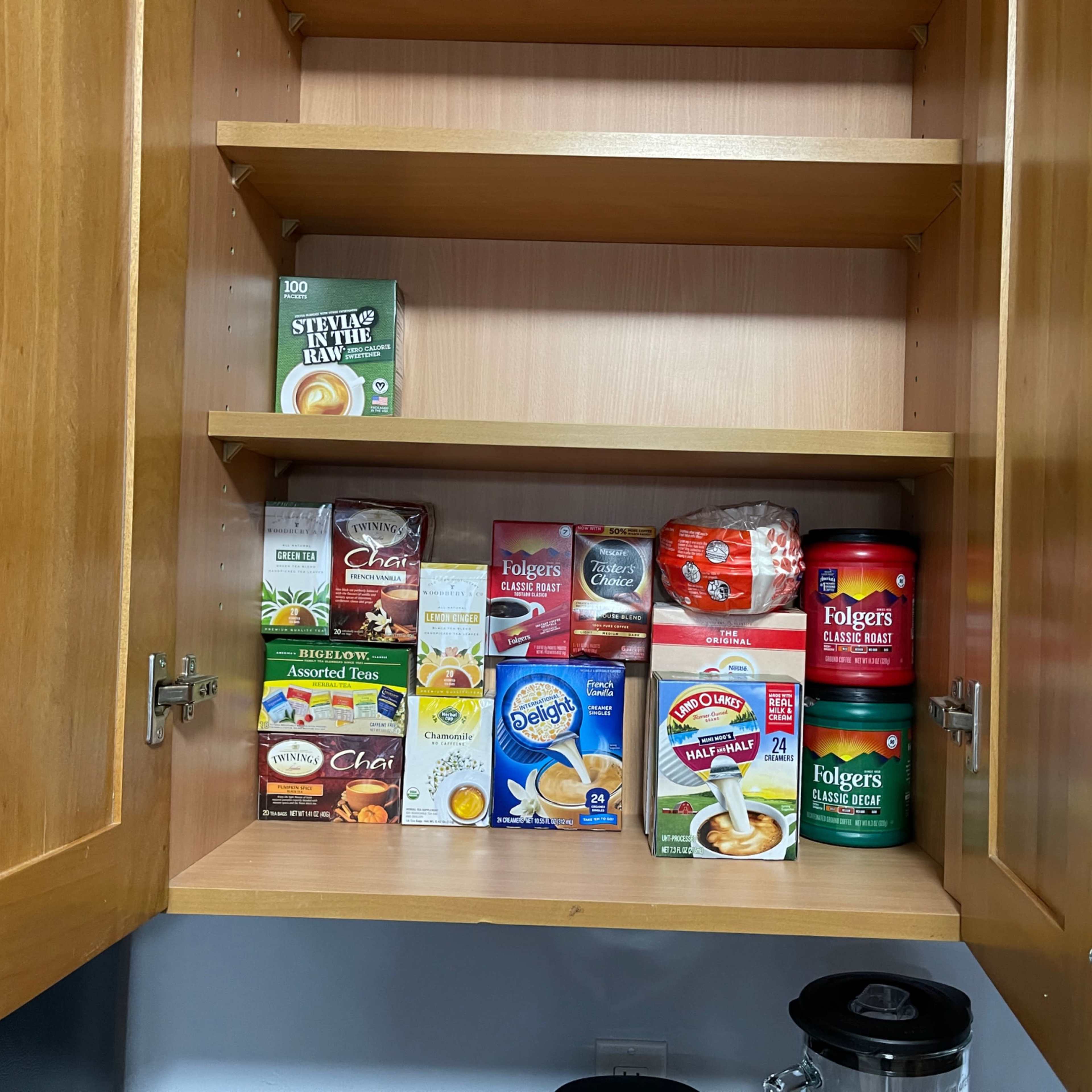 A kitchen cabinet shelf filled with various boxes and containers of tea, coffee, and sweeteners.