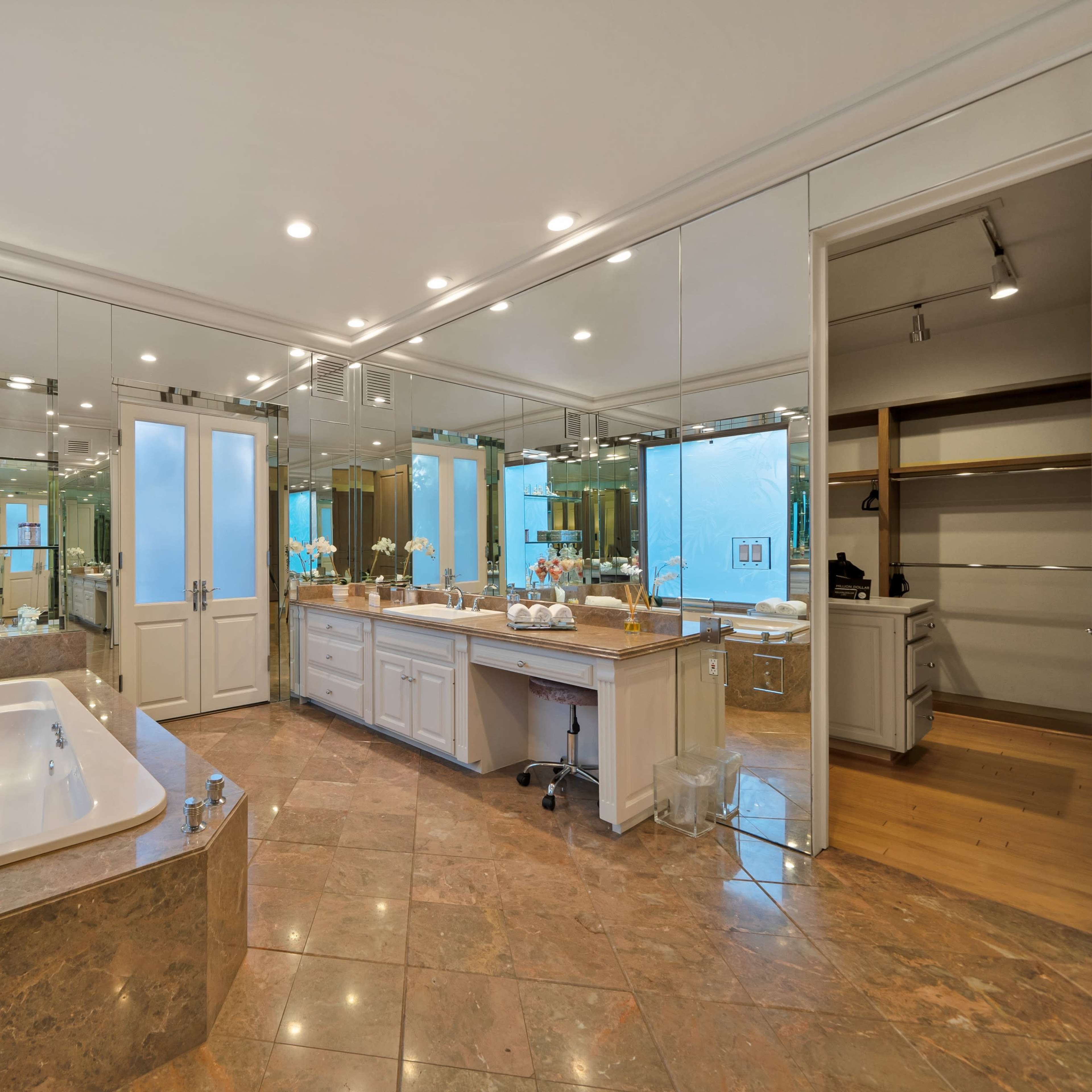 A spacious bathroom featuring a large bathtub, dual sinks with a countertop, and a wall of mirrors reflecting natural light.