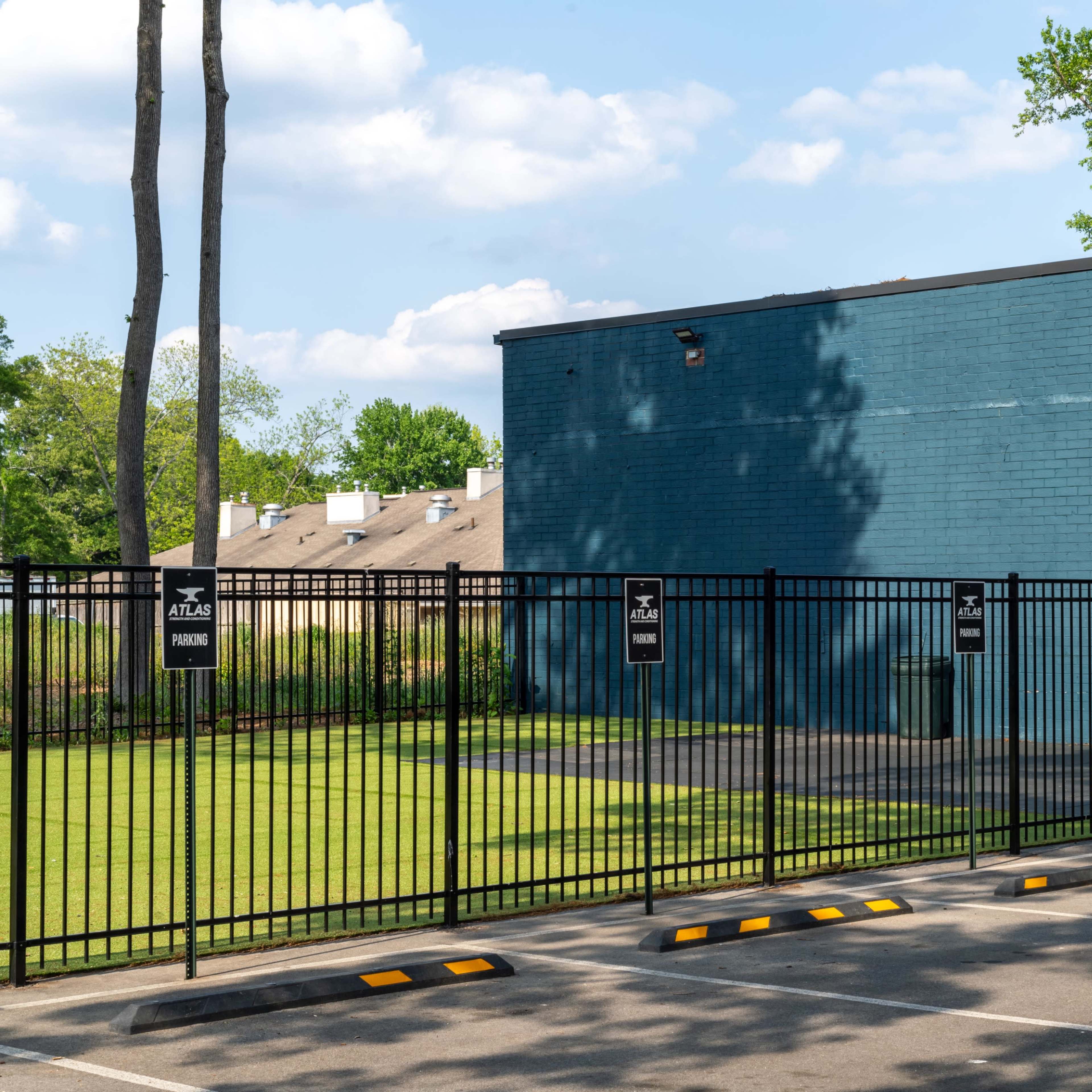 A blue brick building with a fenced-in area and parking spaces is visible under a partly cloudy sky.