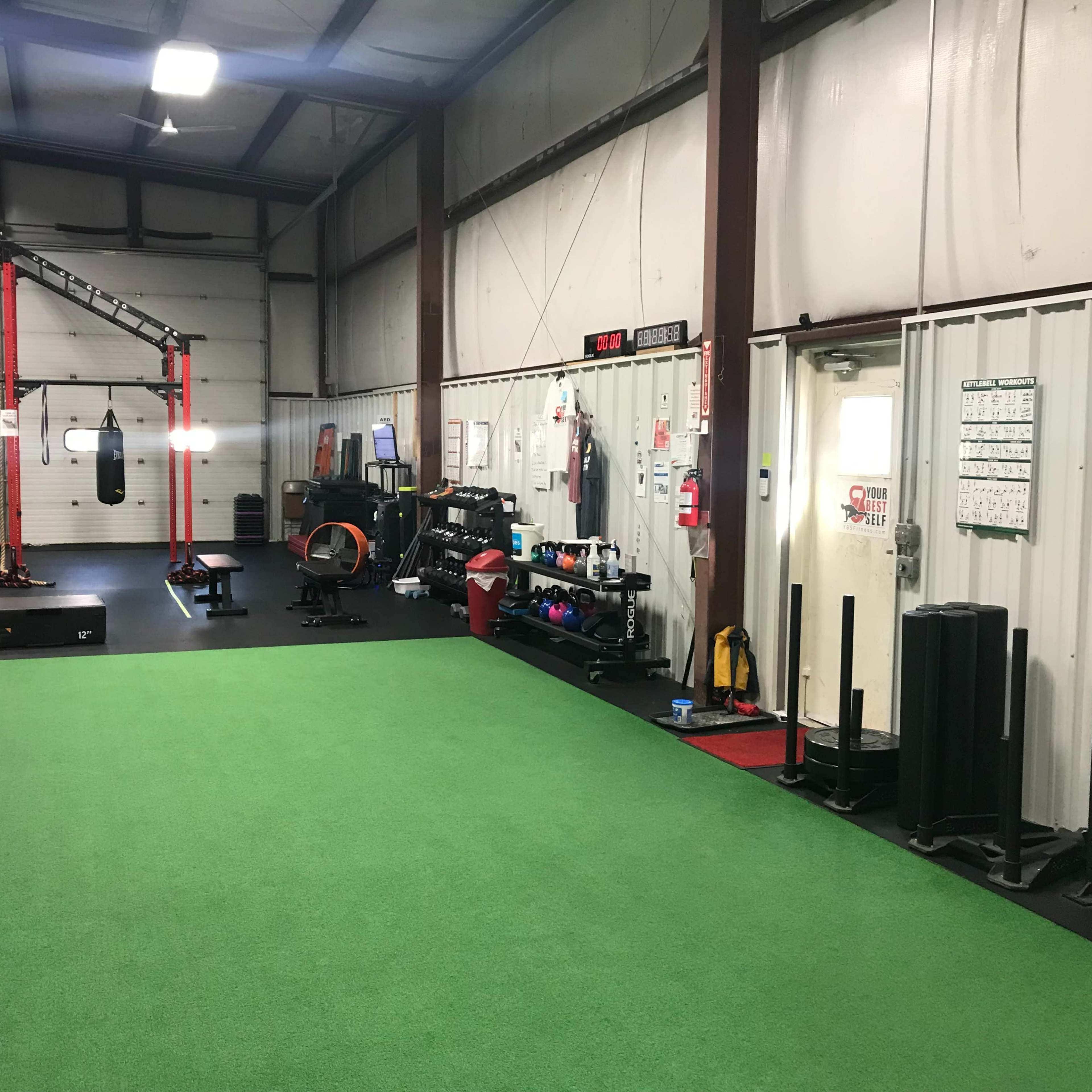 A gym interior with green turf flooring, exercise equipment, and a boxing bag suspended from a frame.