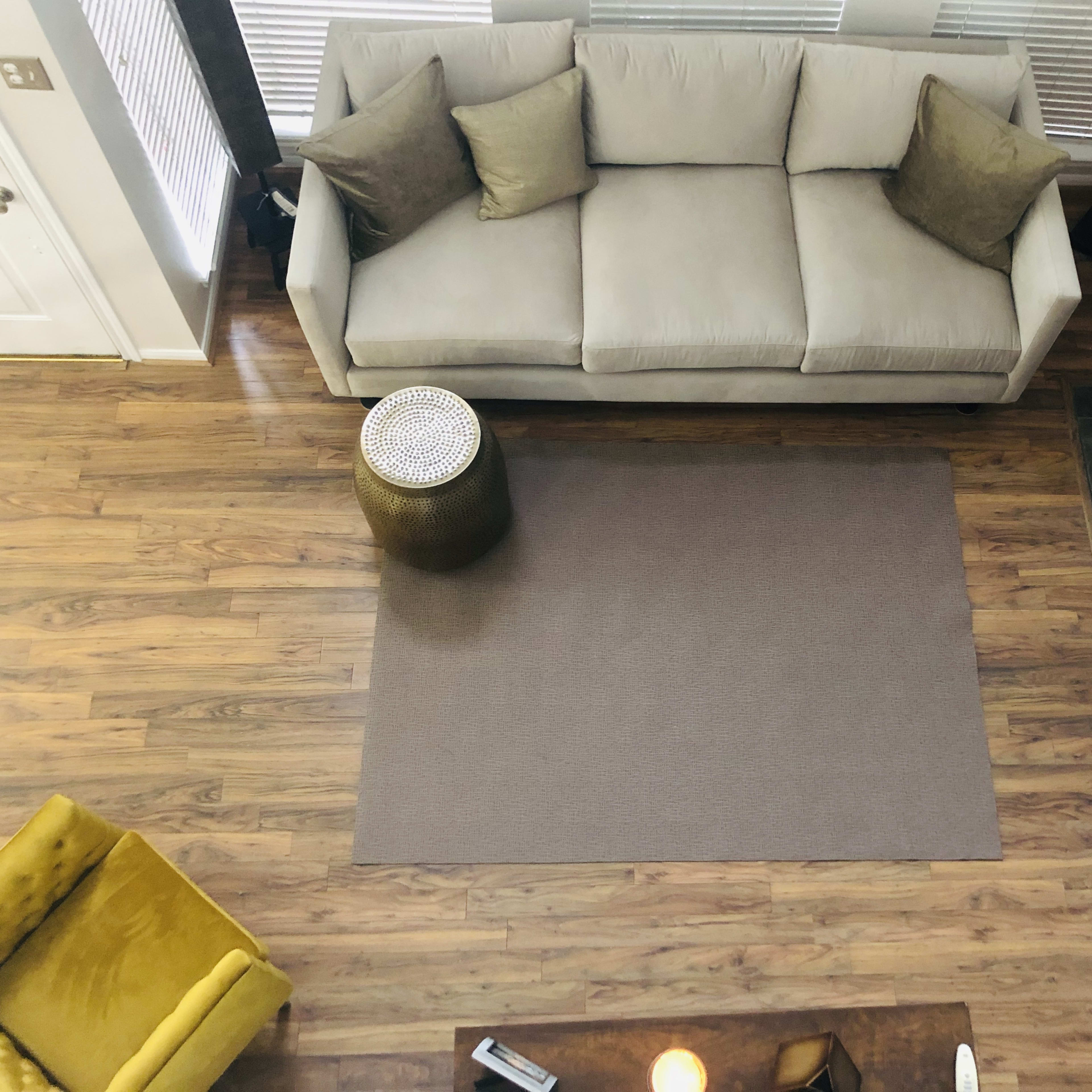 A spacious living room with a beige sofa, a round metallic side table, a light brown rug, and a fireplace.
