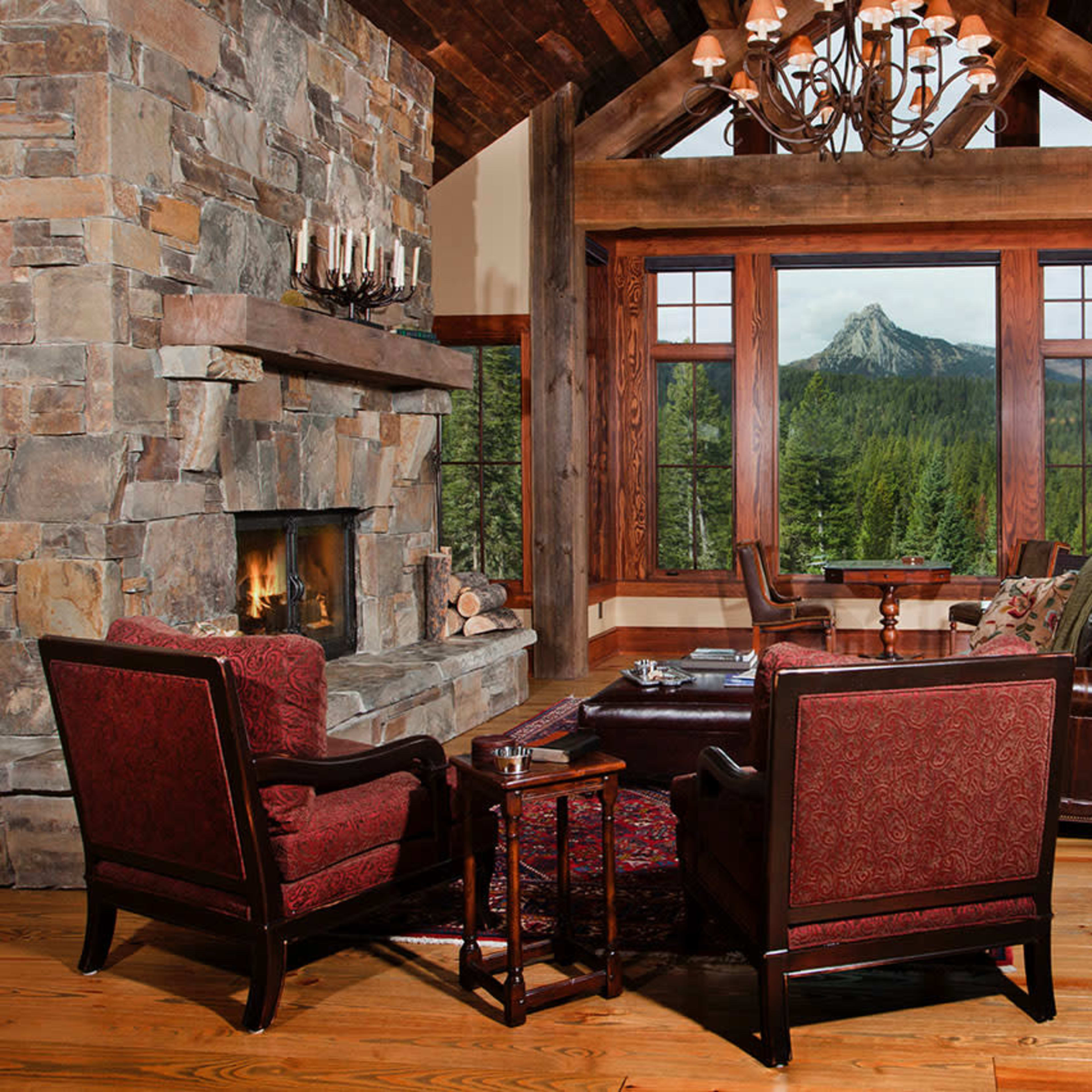 A spacious living room features a stone fireplace, large windows showcasing a mountain view, and leather seating arranged around a wooden coffee table.