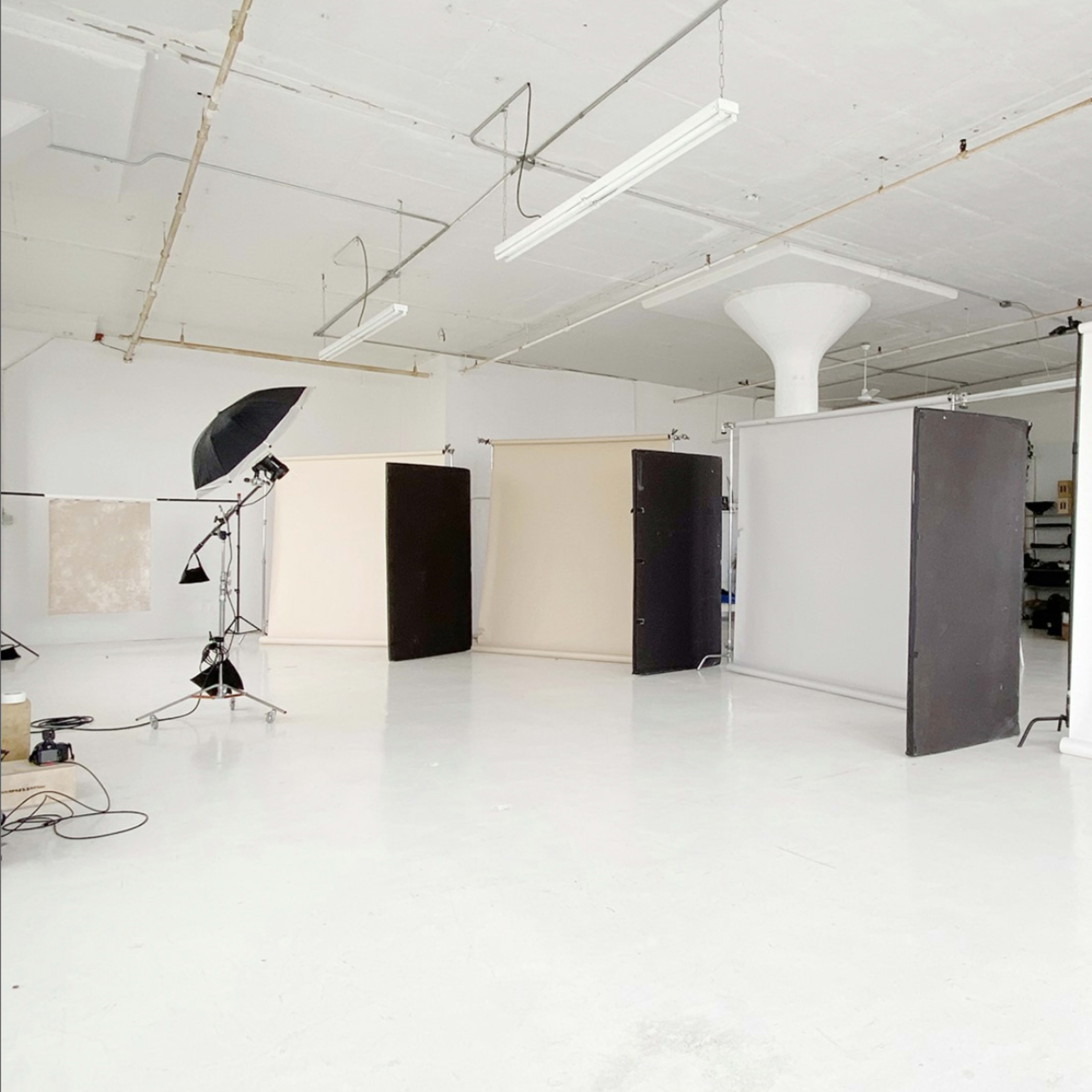 A spacious photography studio with several backdrop stands and lighting equipment arranged on a white floor.
