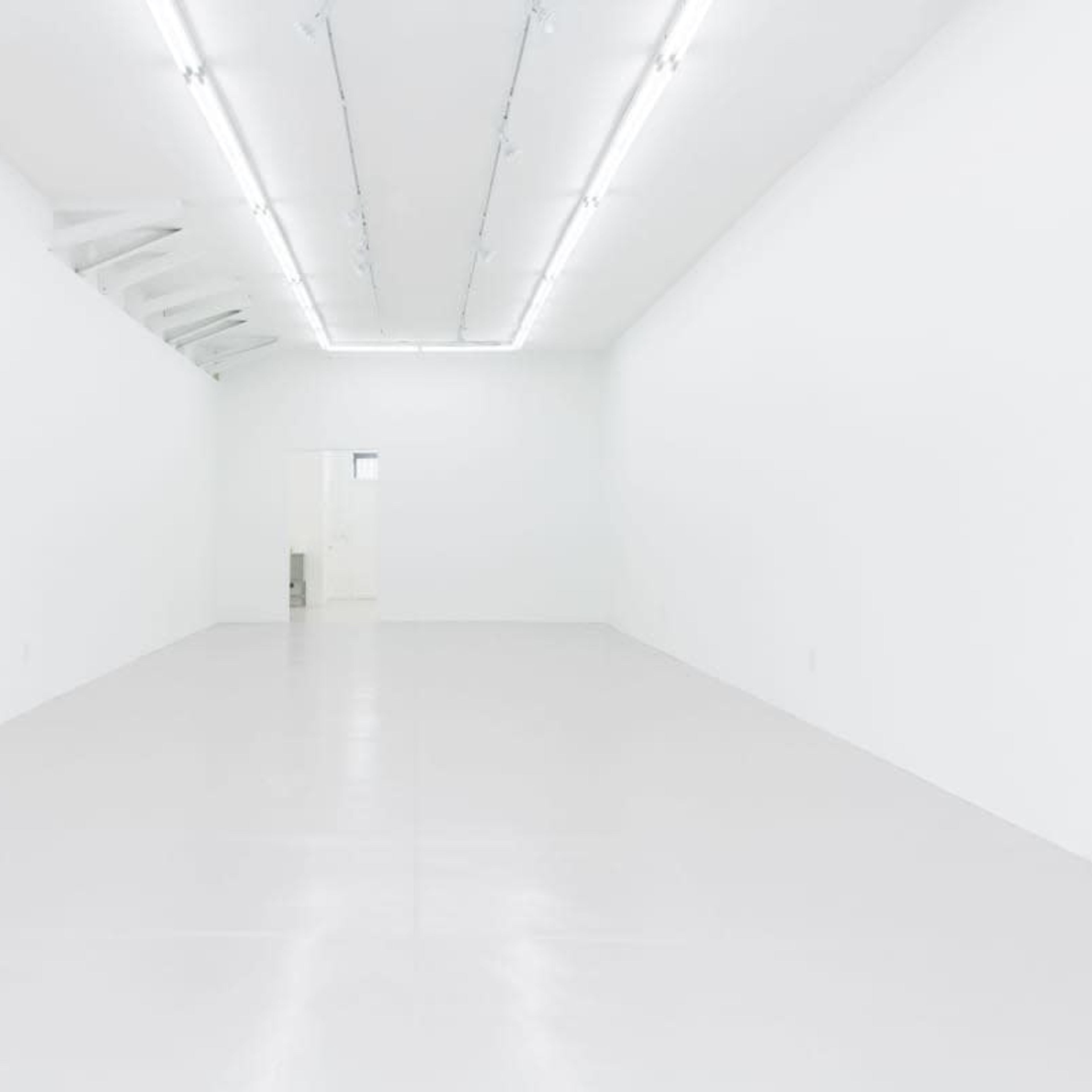 An empty, white-walled room with a smooth, light-colored floor and fluorescent lighting.
