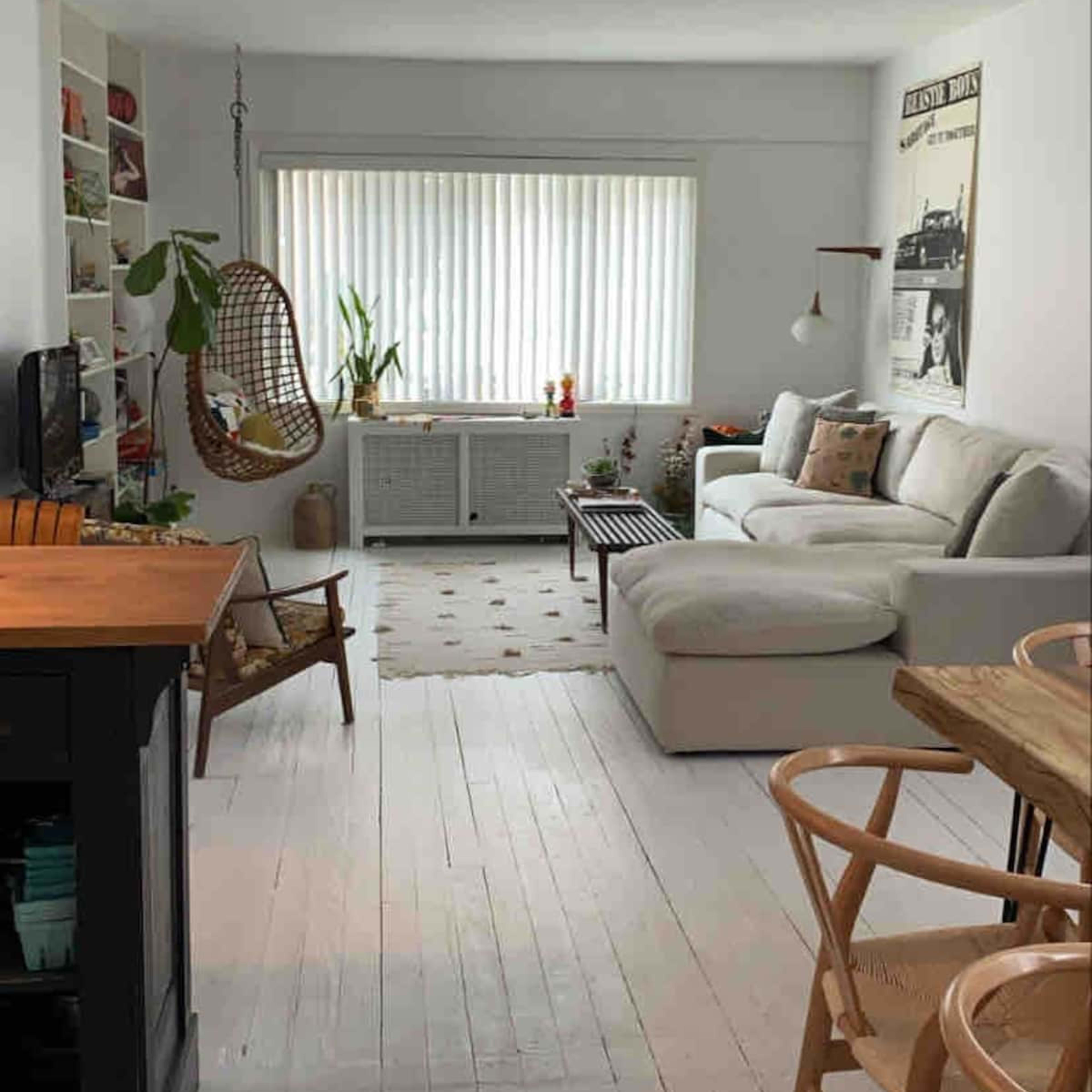 A bright, open living space featuring a white sofa, a hanging chair, and a wooden dining table surrounded by chairs.