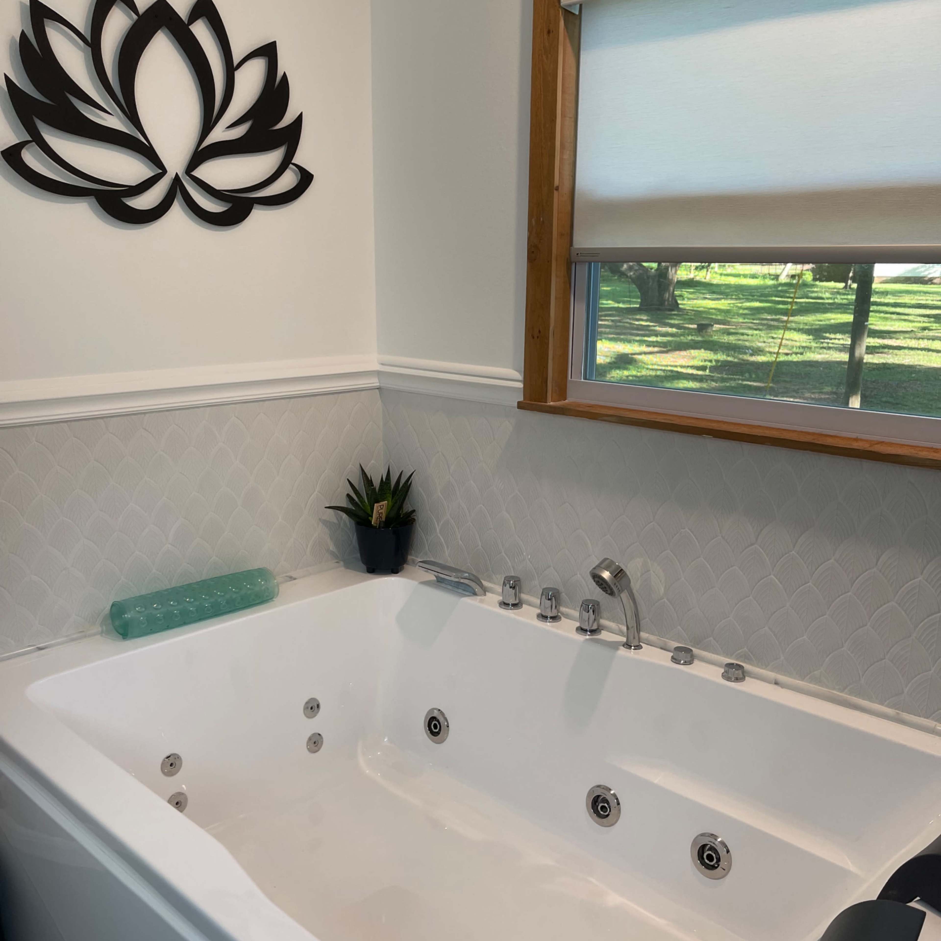 A modern Jacuzzi bathtub situated against a wall with a window and a decorative lotus flower above it.