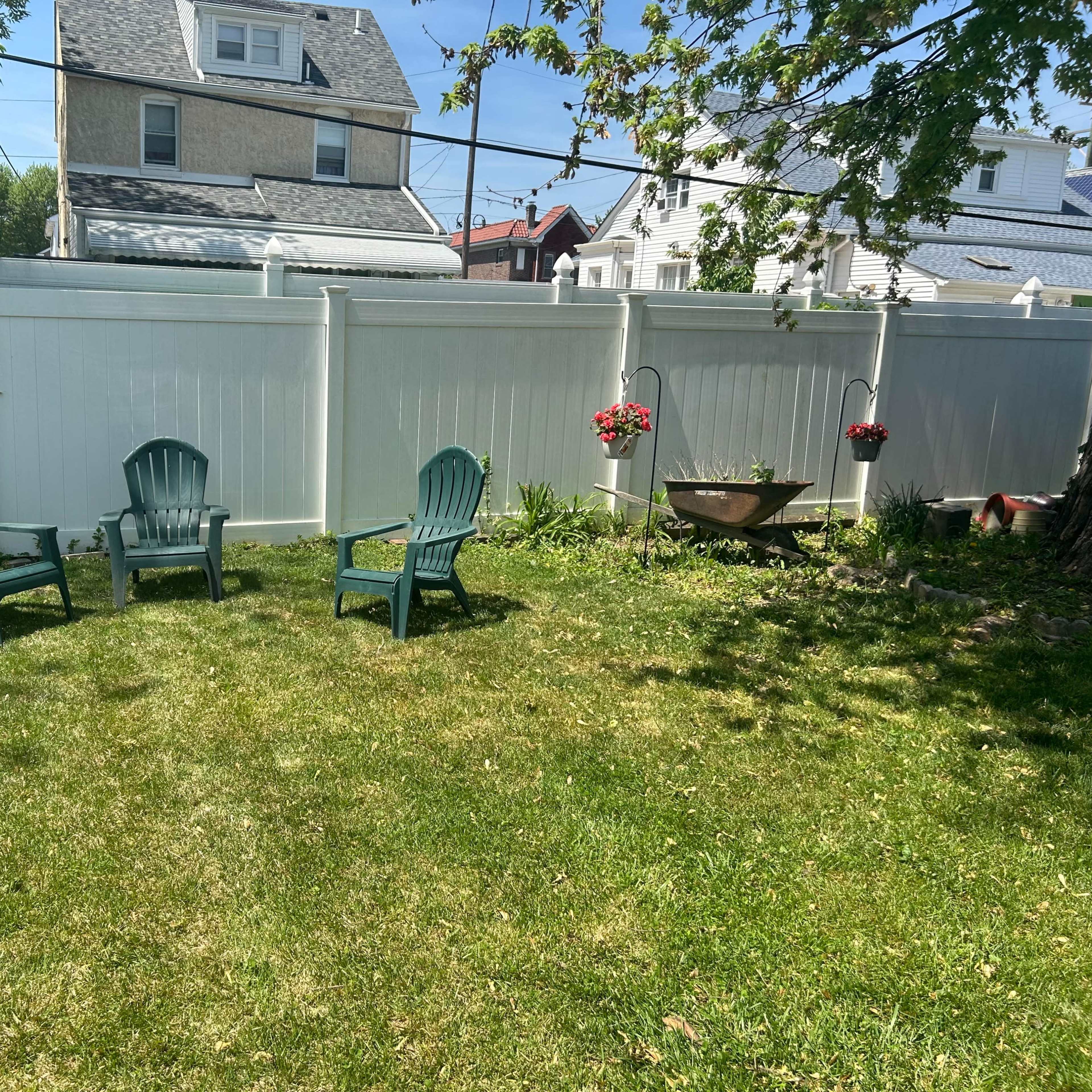 A grassy backyard features five green chairs arranged in a semicircle near a decorative planter and a white fence.