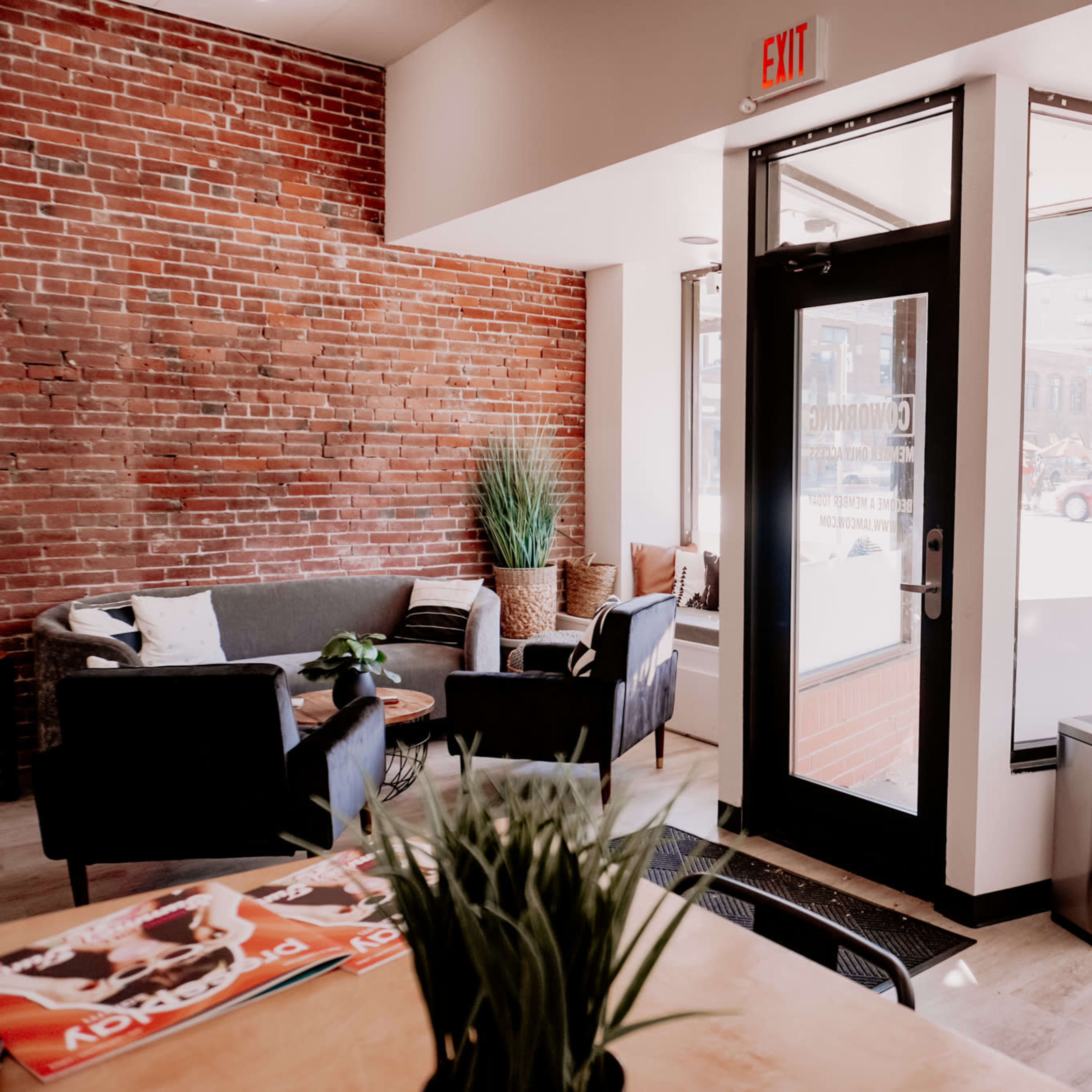 A cozy café interior with exposed brick walls, seating areas featuring sofas and chairs, and large windows allowing natural light in.