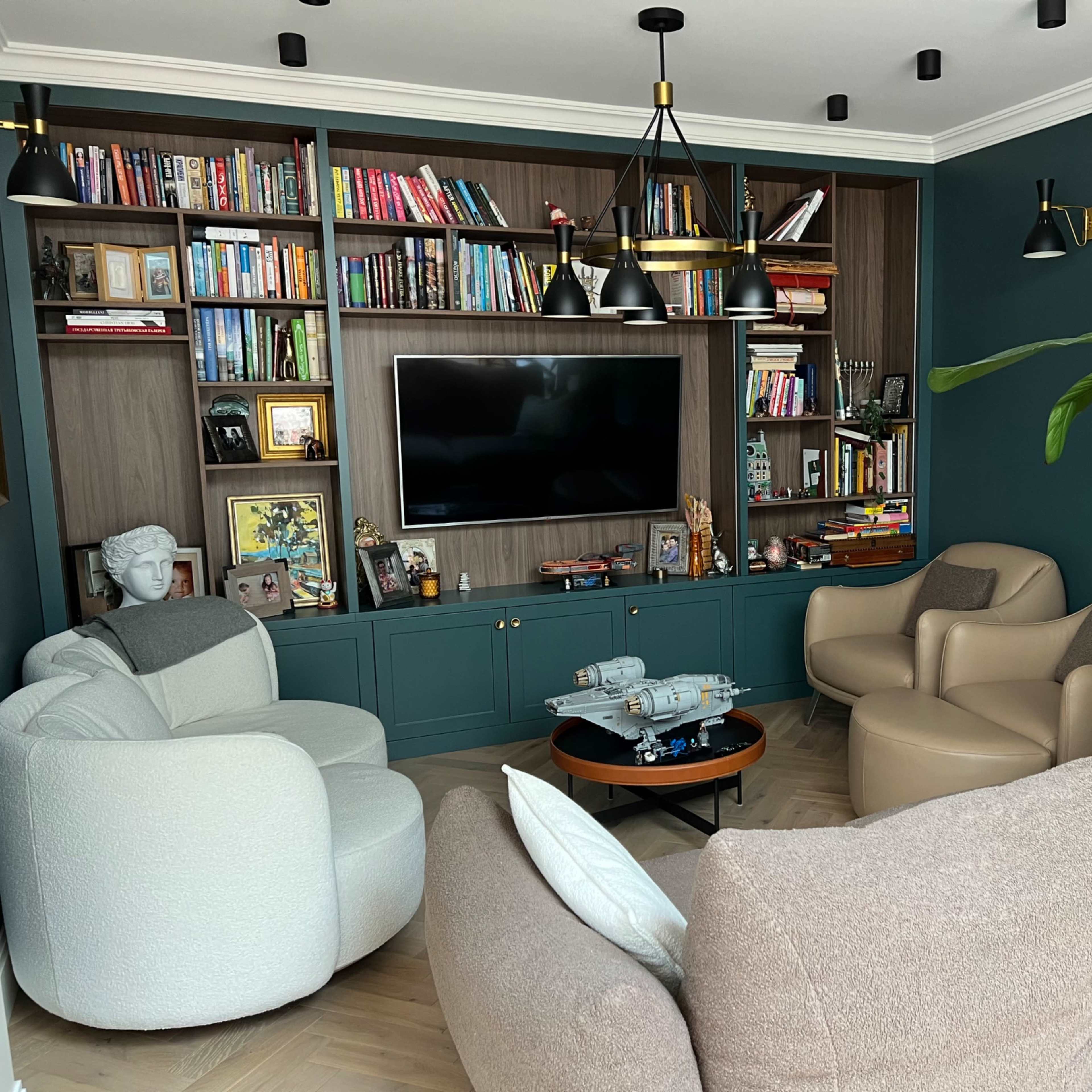 A cozy living room features a wall of bookshelves, a television, and two distinct seating areas with modern armchairs and a round coffee table.