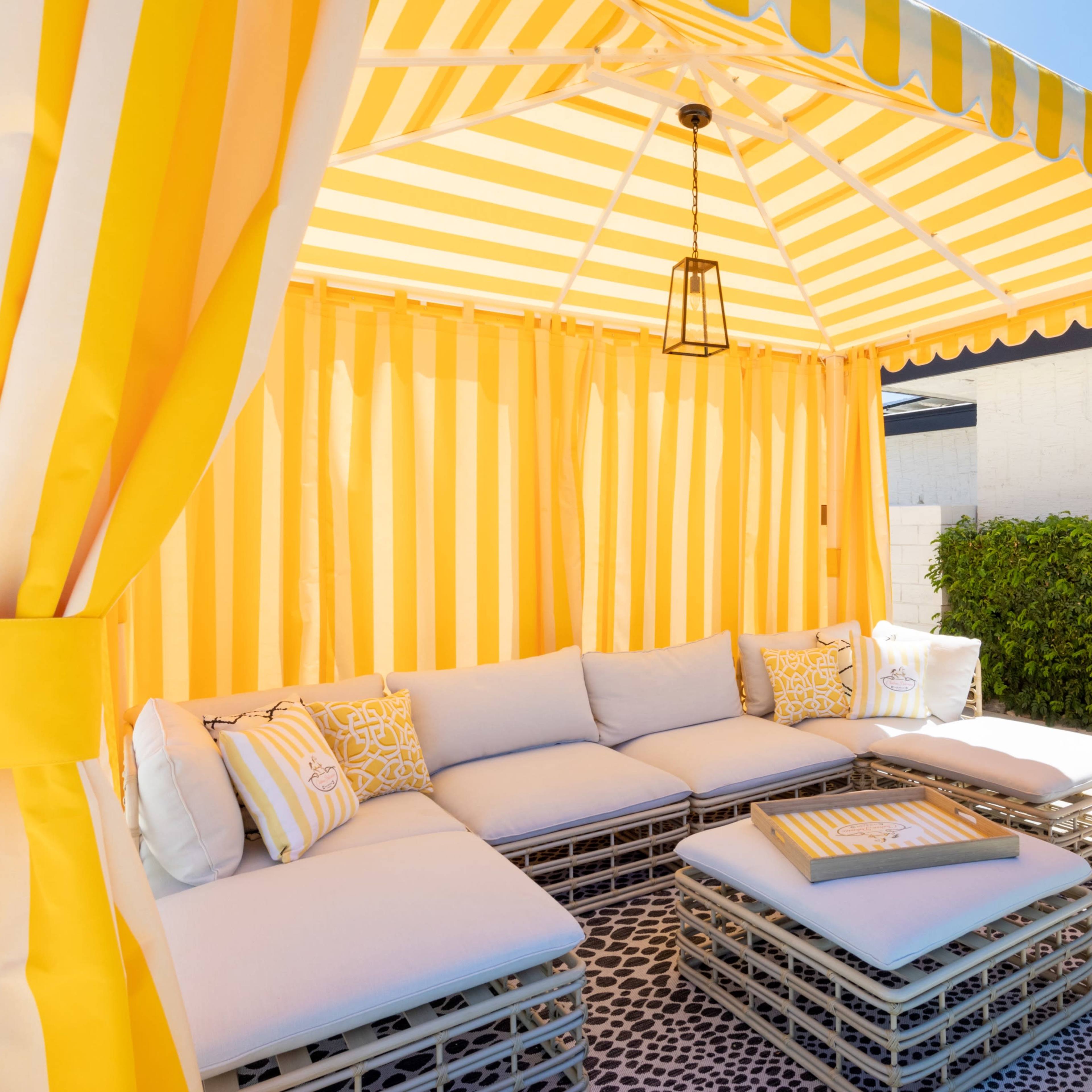 A yellow and white striped outdoor cabana with a cushioned seating area and a small coffee table.