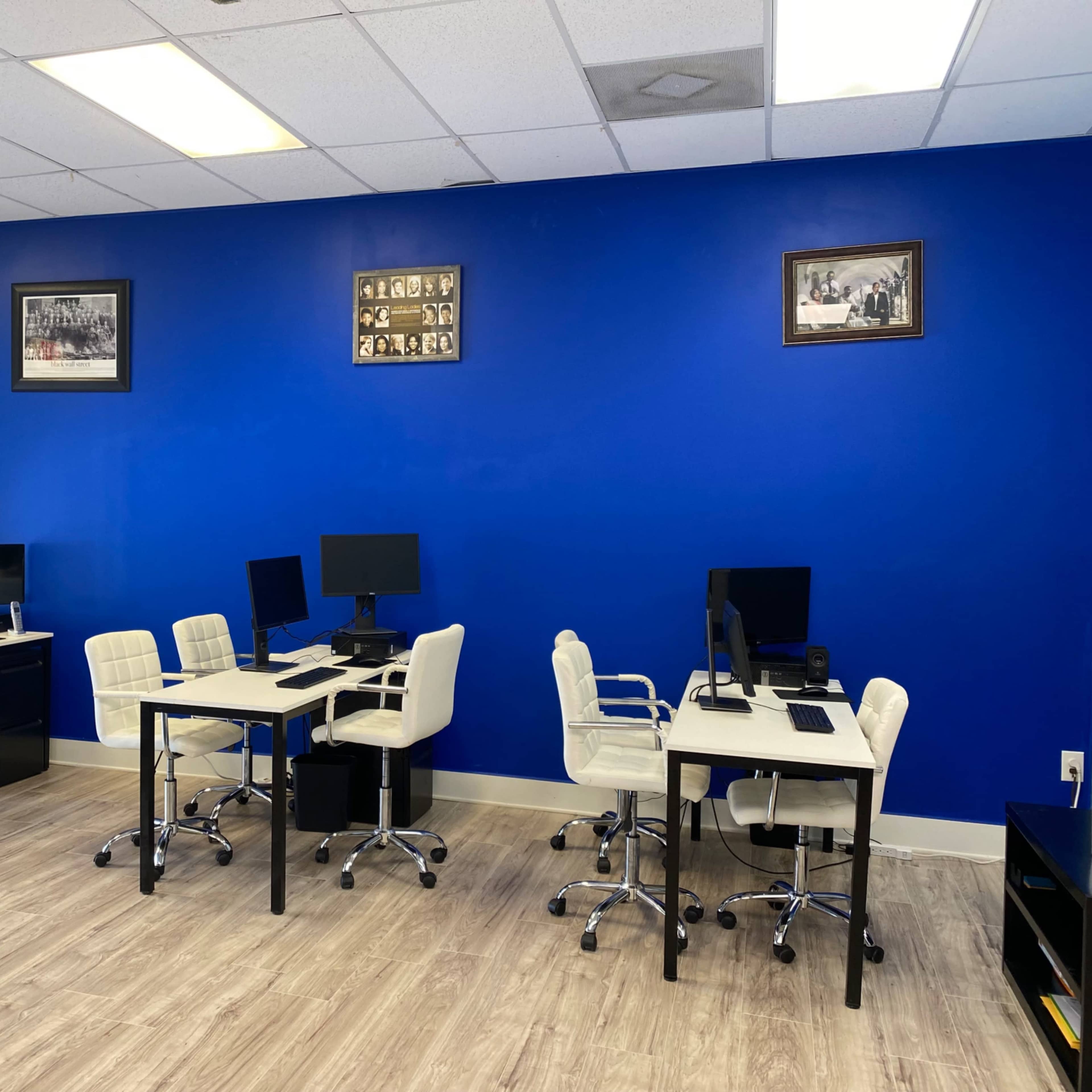 A bright blue office space with multiple white desks and computer stations arranged on a light wood floor.