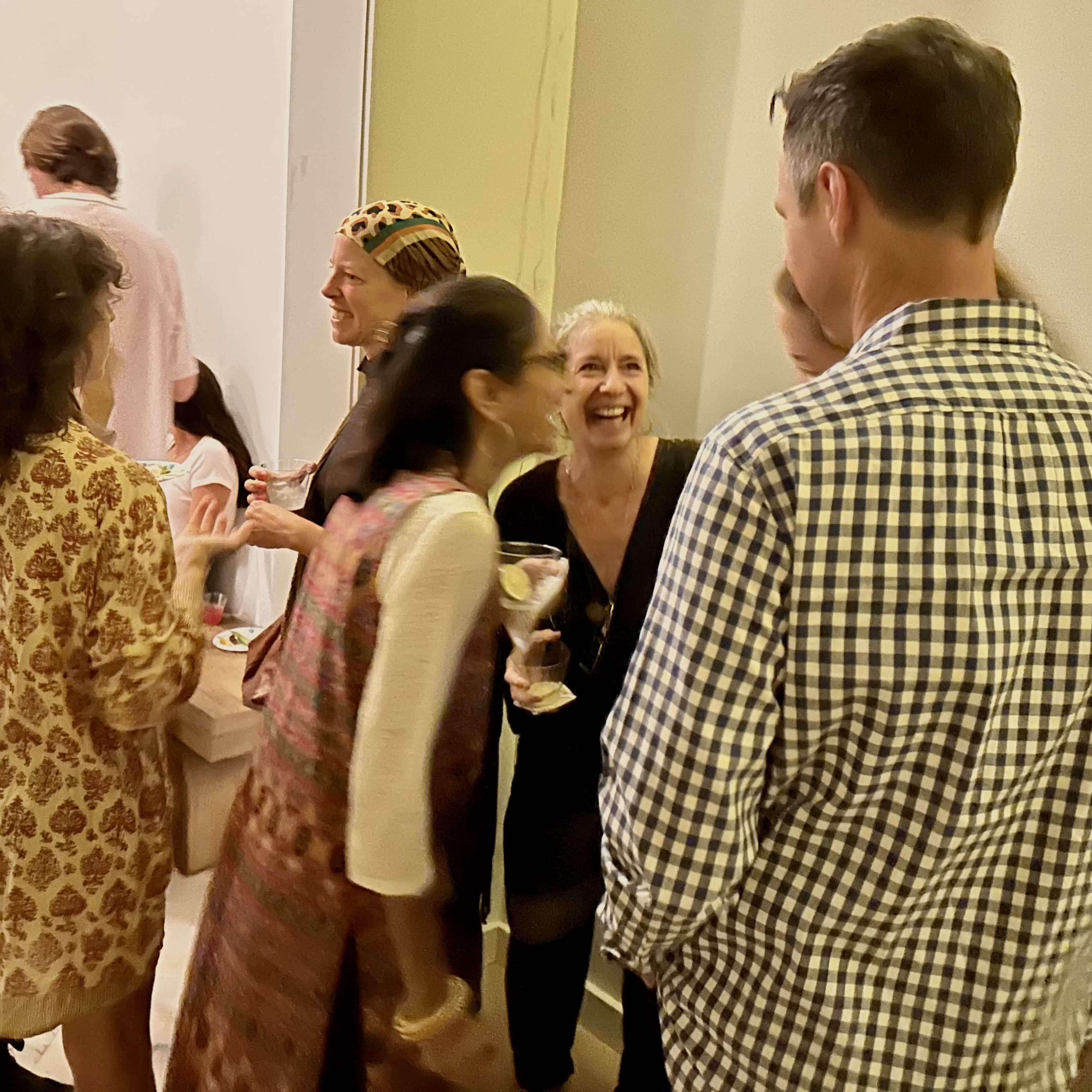 A group of people socialize at a gathering, with some holding drinks and others engaging in conversation.