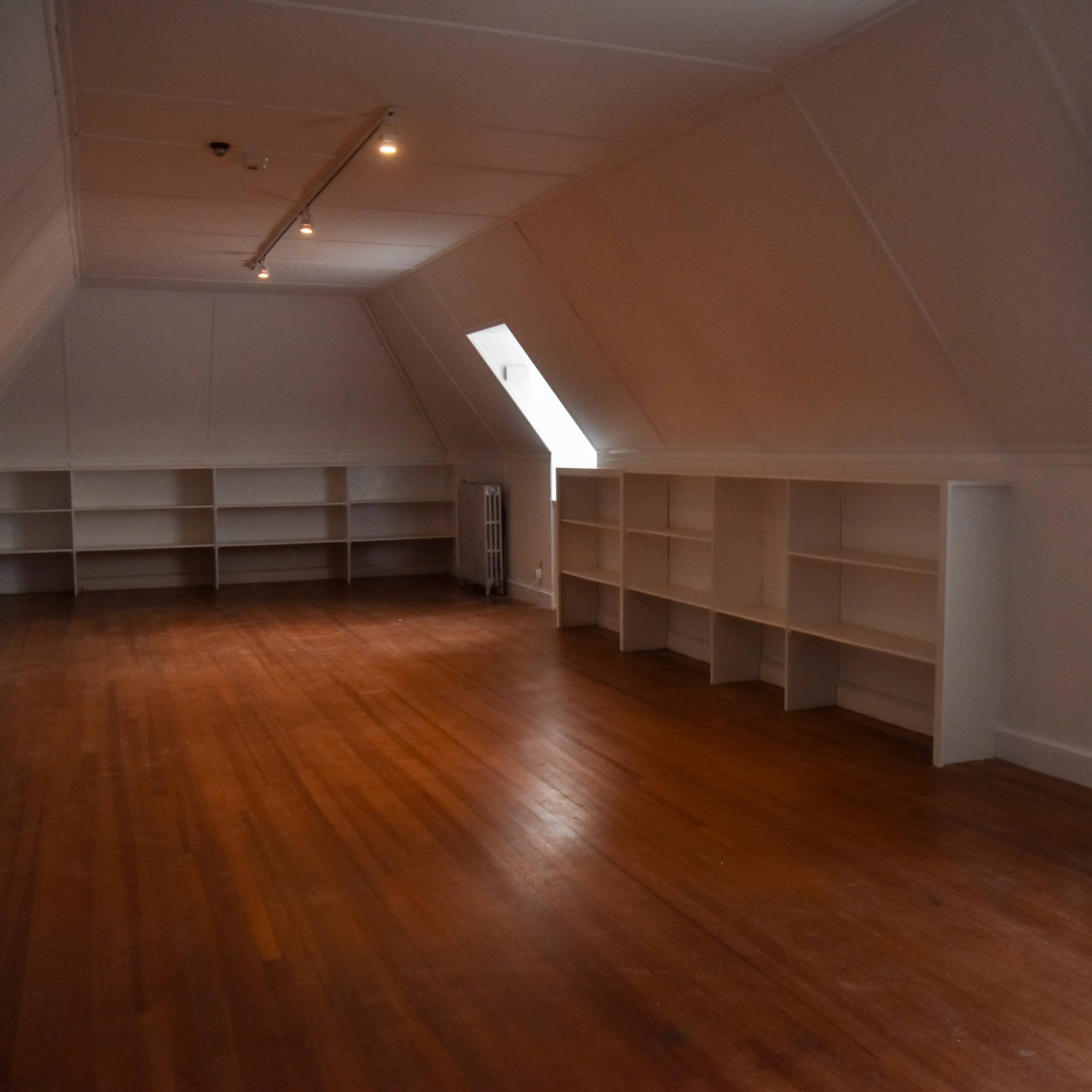 A spacious, empty attic room with slanted ceilings, wooden floors, and built-in shelves along the walls.