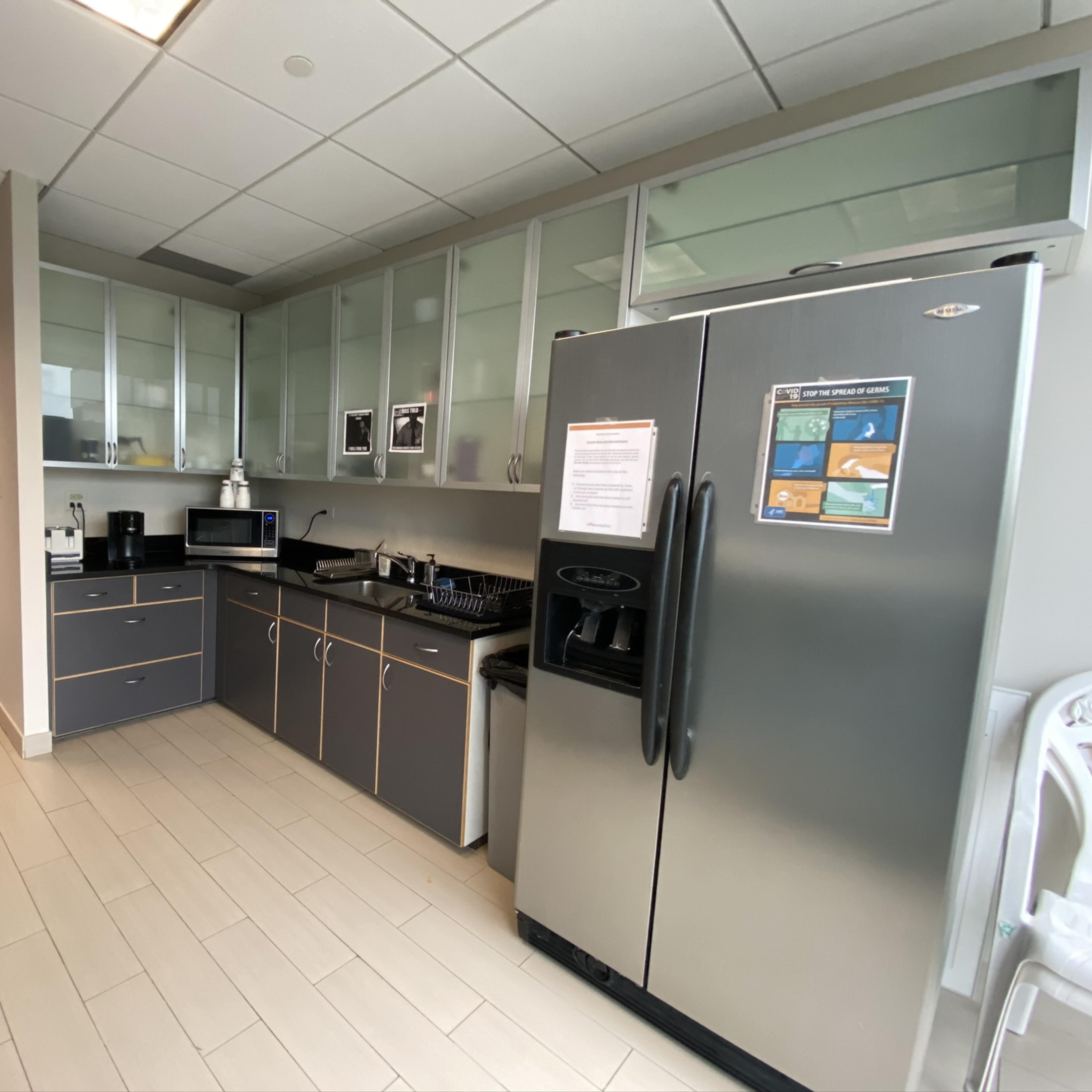 A modern kitchen area with gray cabinetry, a refrigerator, a microwave, and kitchenware neatly arranged on a countertop.
