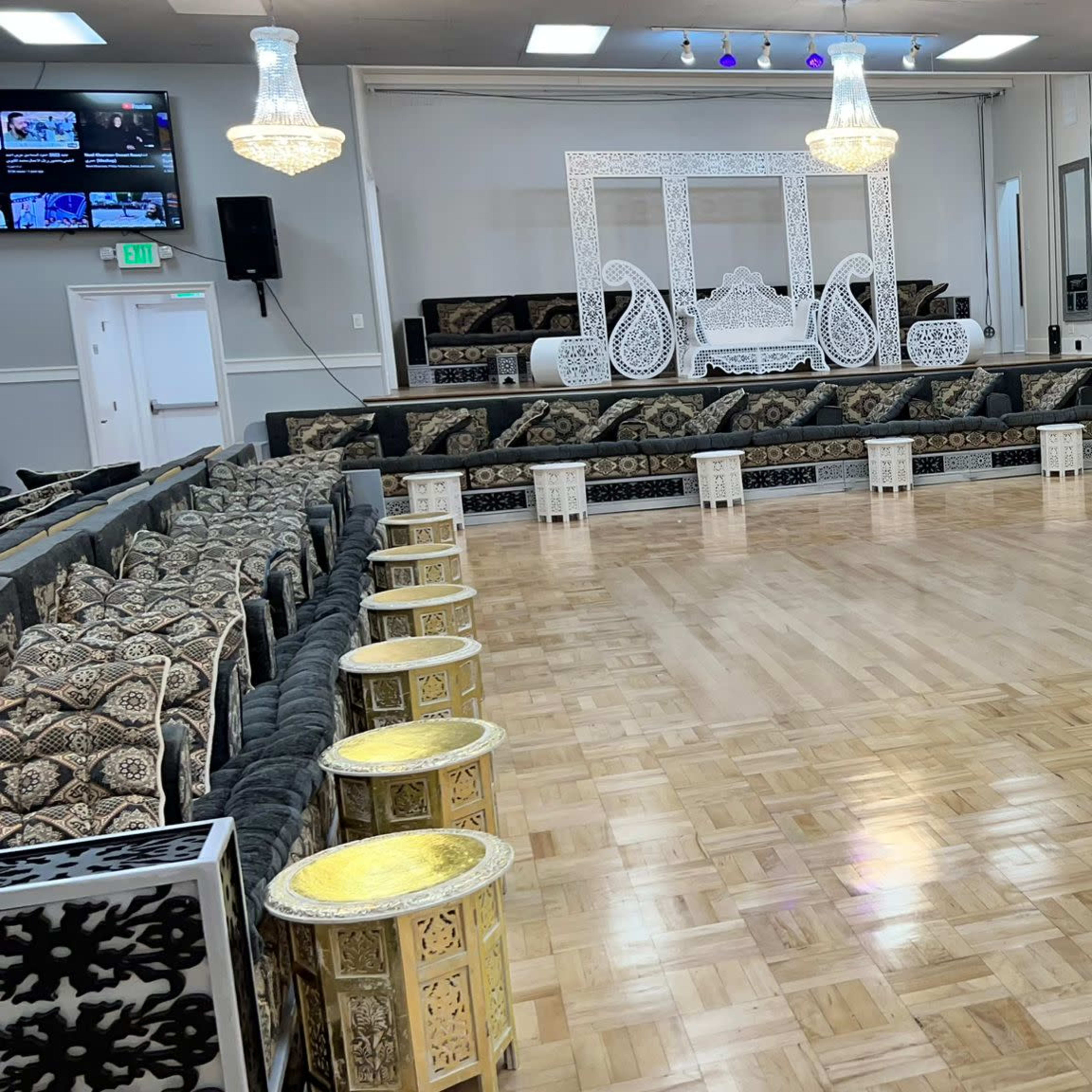 A spacious event hall with polished wooden flooring surrounded by ornate black and gold seating arrangements and small tables.