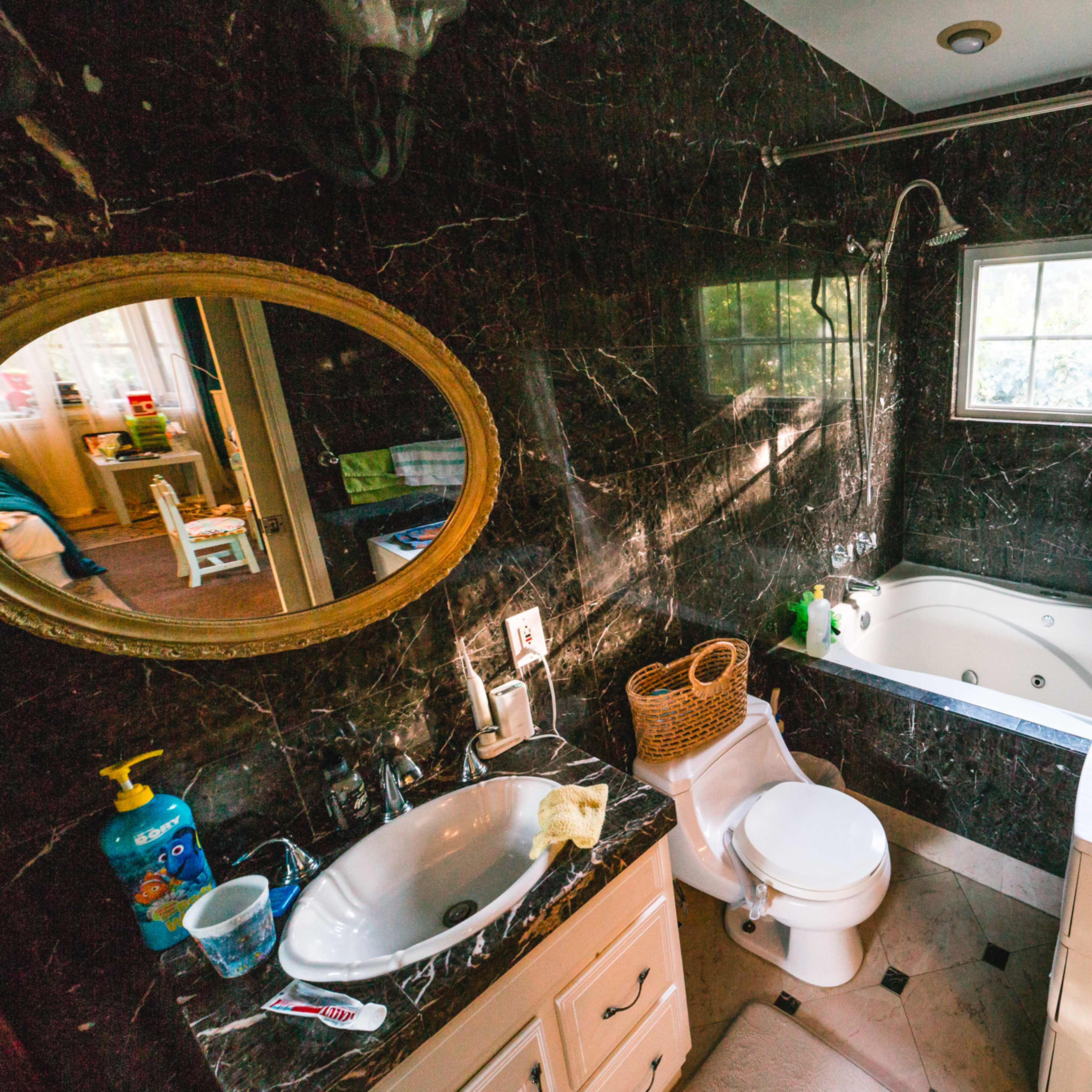 A bathroom featuring a dark marble design with a bathtub, a toilet, a sink, and a window allowing natural light.