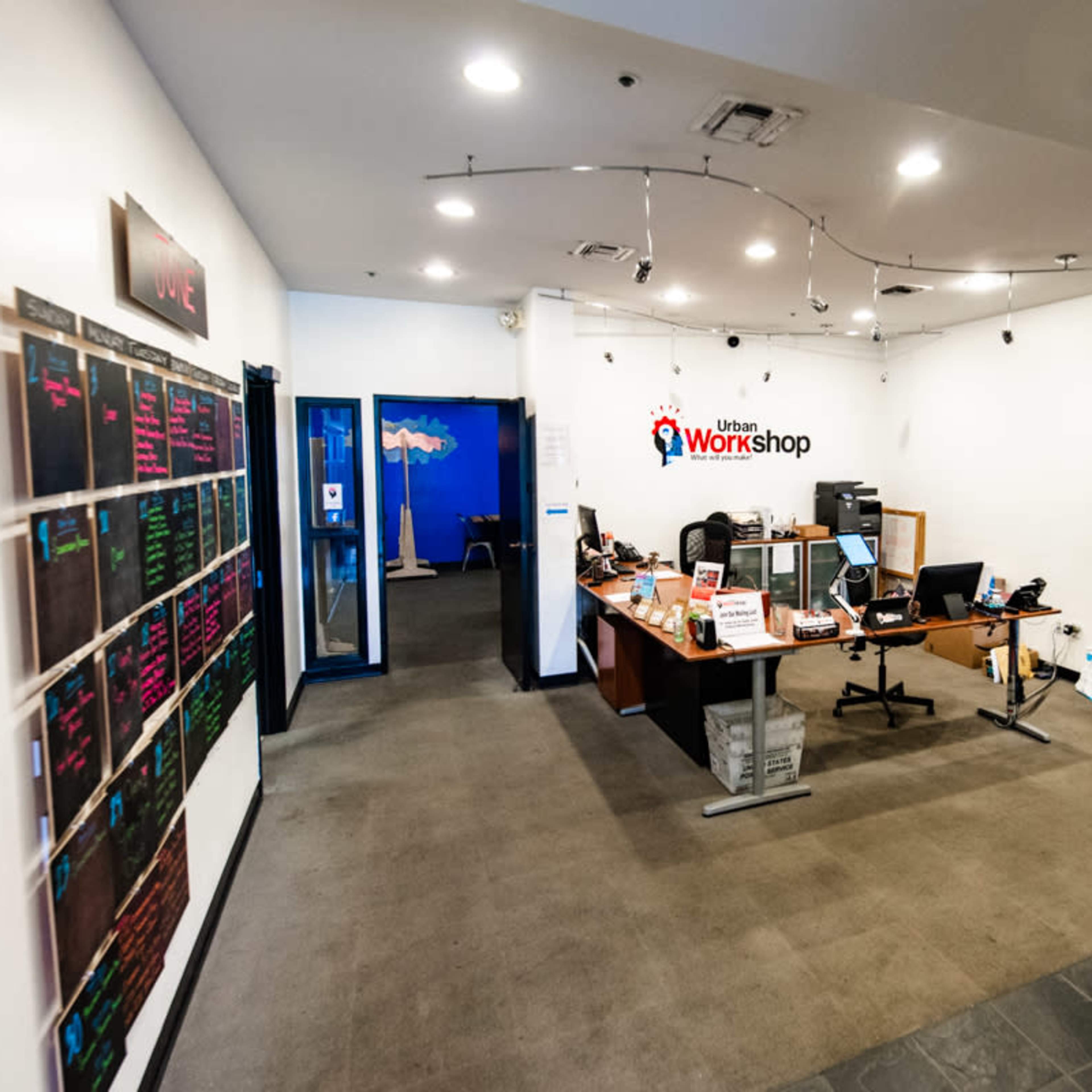 A modern office space with a reception area featuring a desk and a colorful wall mural, alongside a bulletin board displaying information.