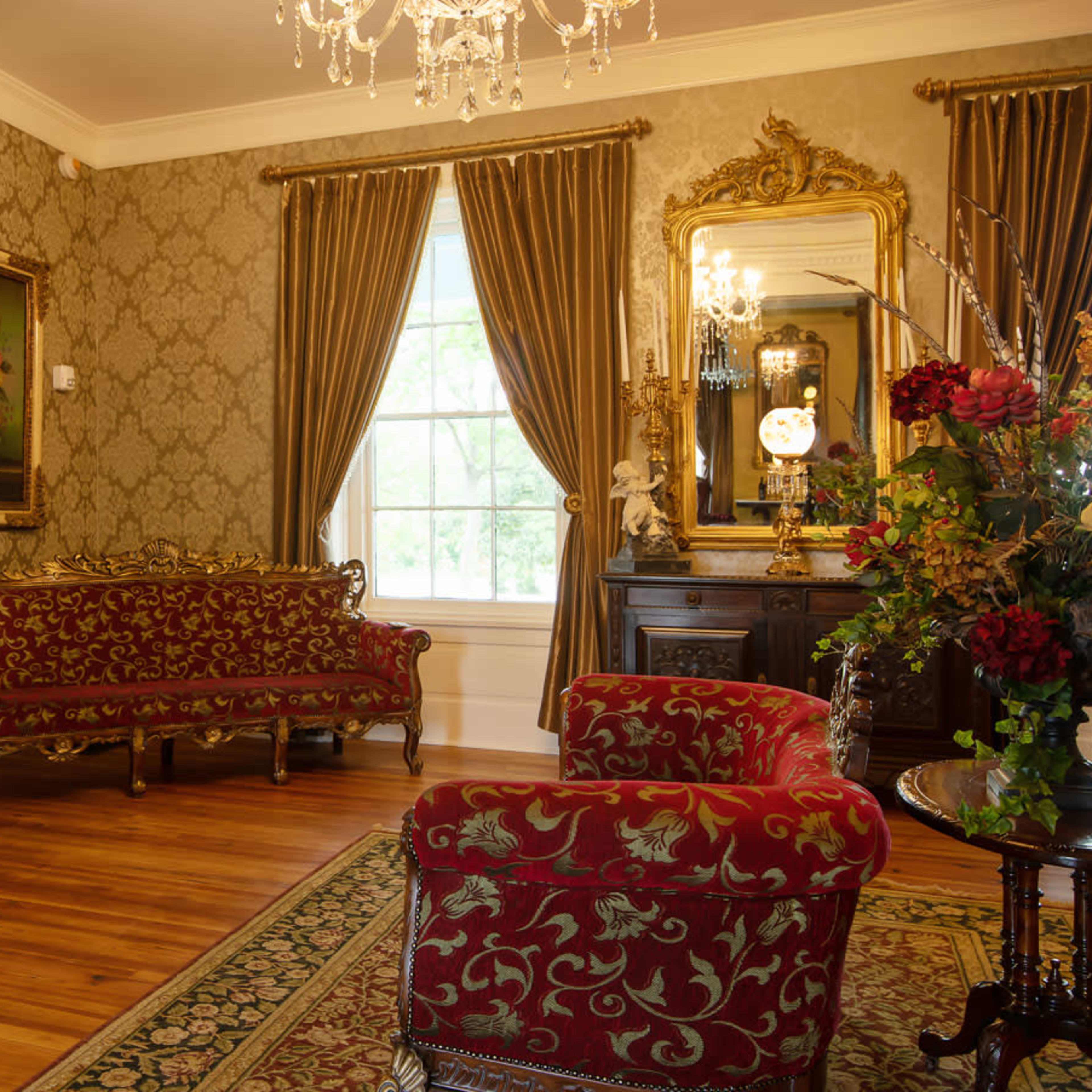 The room features a decorative fireplace, ornate furniture, and rich floral accents, creating an elegant atmosphere.