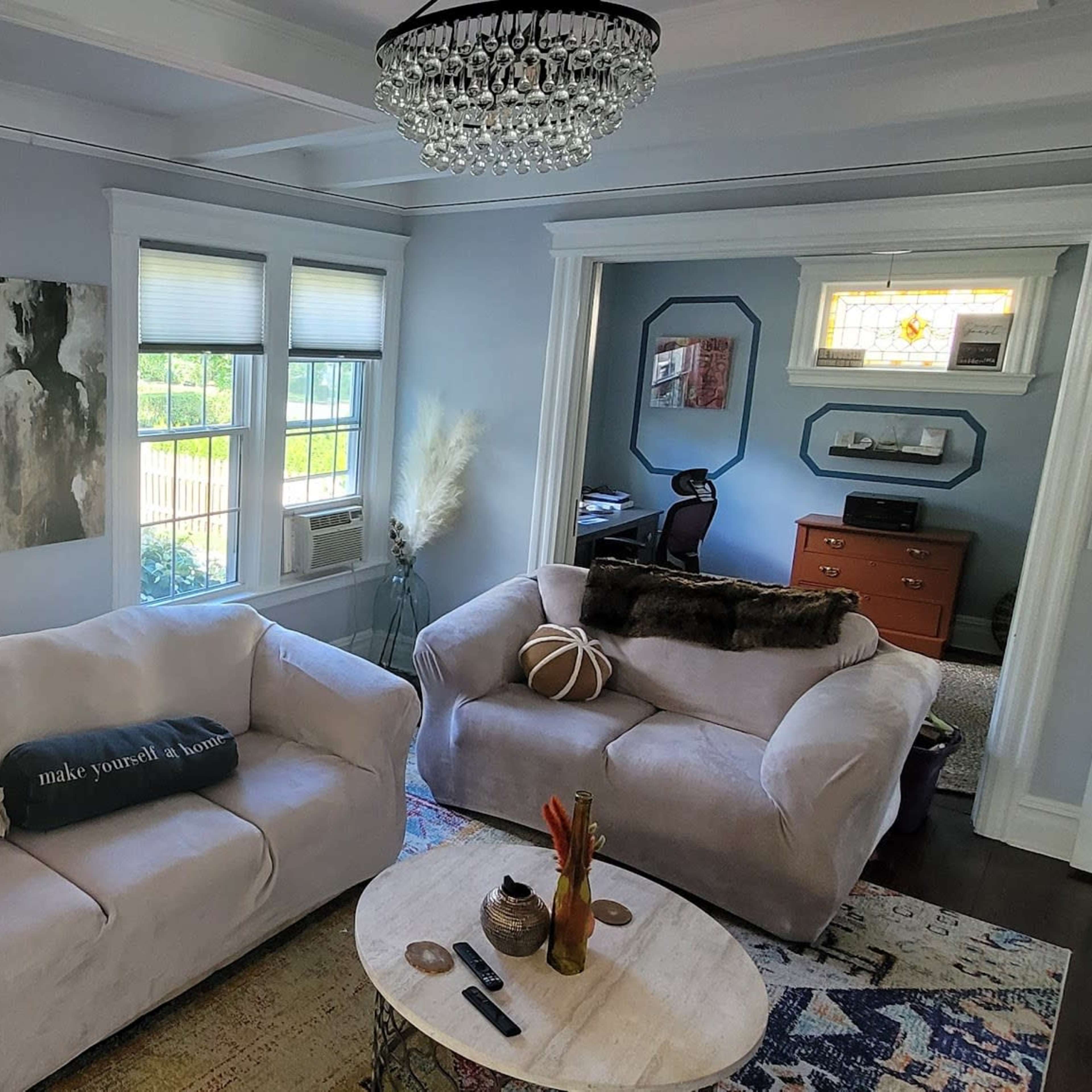 A bright living room features two light-colored sofas, a round coffee table, and large windows that let in natural light.