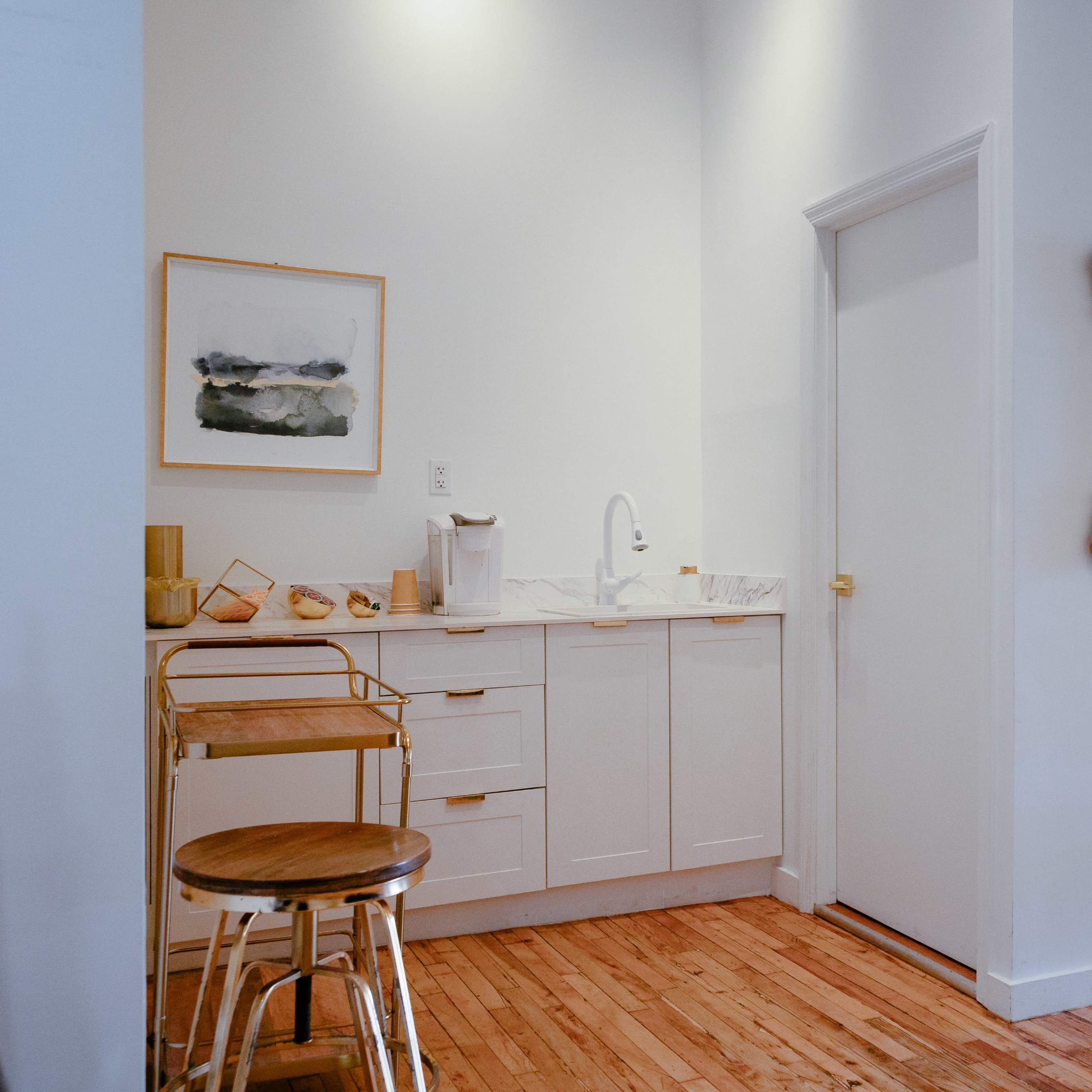 A well-lit corner of a modern kitchen featuring white cabinetry, a small cart, and a decorative mirror on the wall.