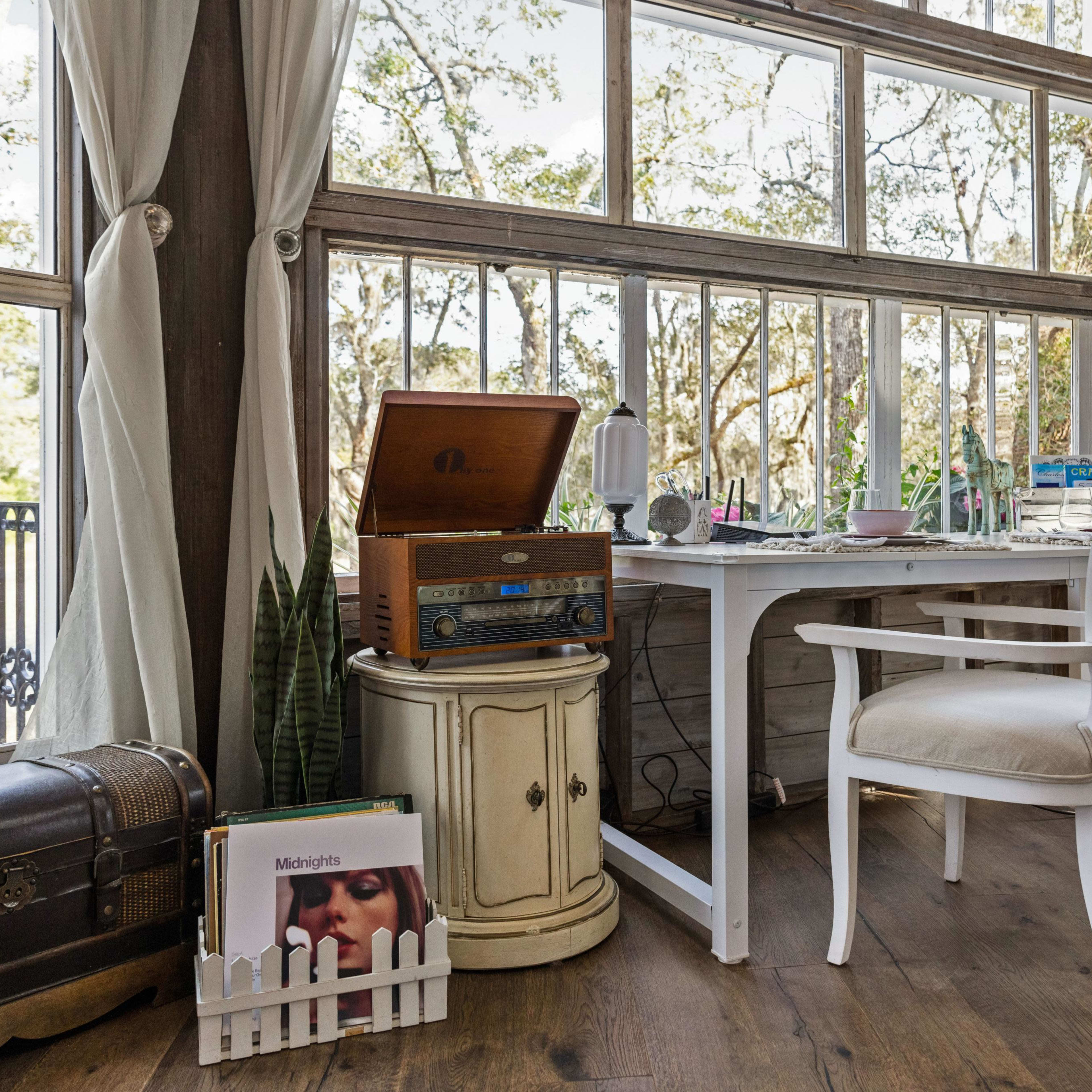 A cozy indoor workspace with a vintage record player, a small table, and a window overlooking a tree-filled landscape.