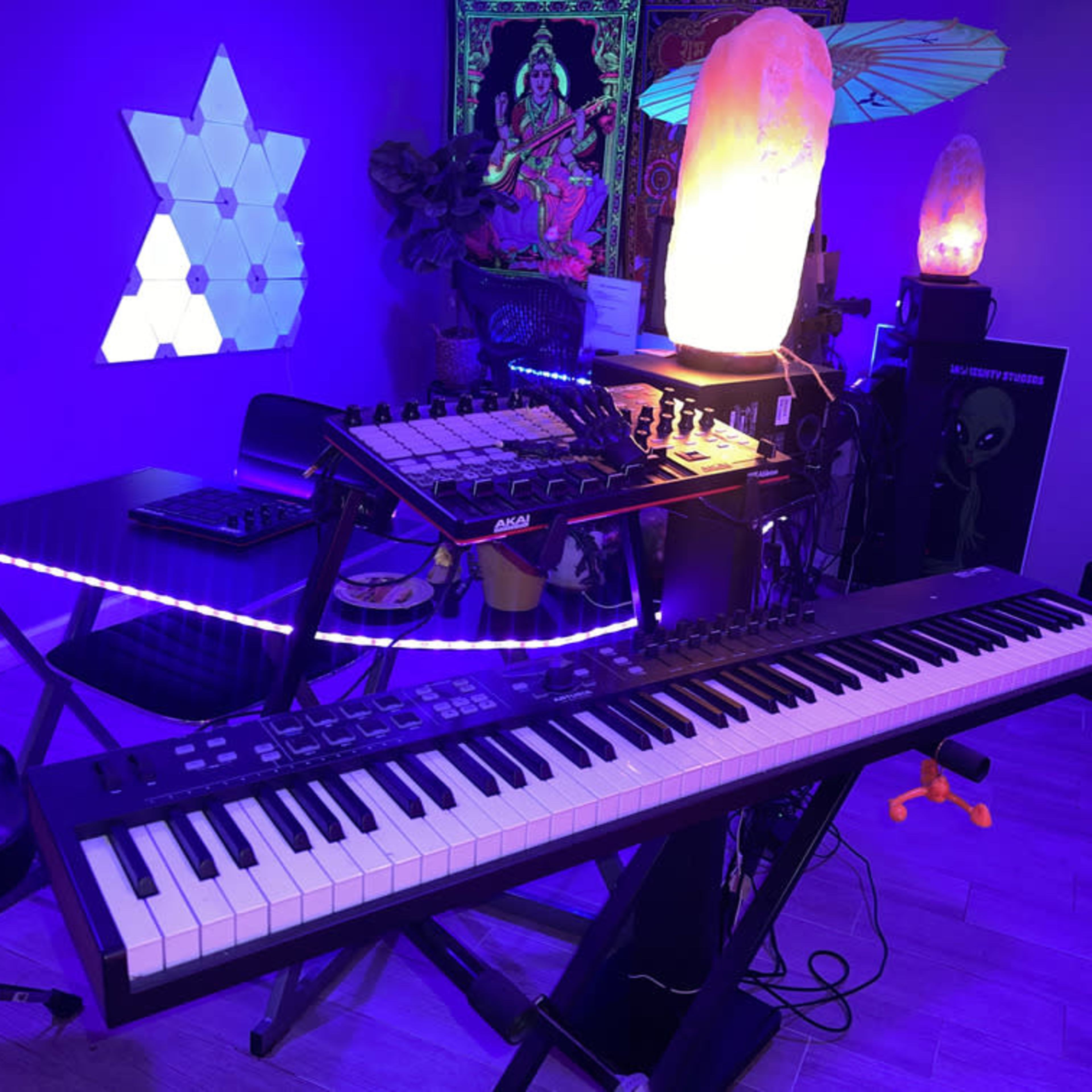 A music production setup featuring a keyboard, a MIDI controller, ambient lighting, and decorative elements in a vibrant room.