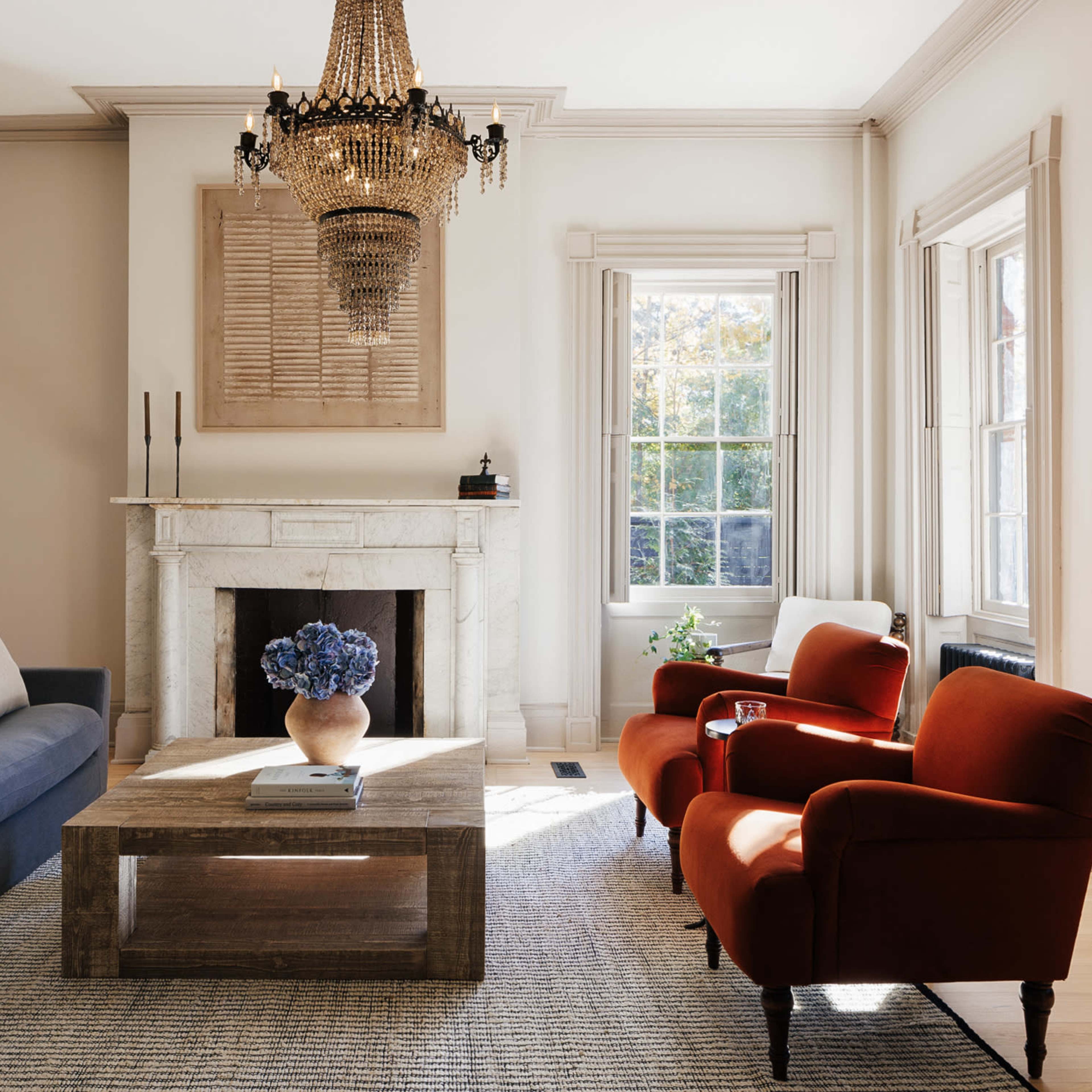 The living room features a blue sofa, two red armchairs, a wood coffee table, and a chandelier above a stone fireplace.