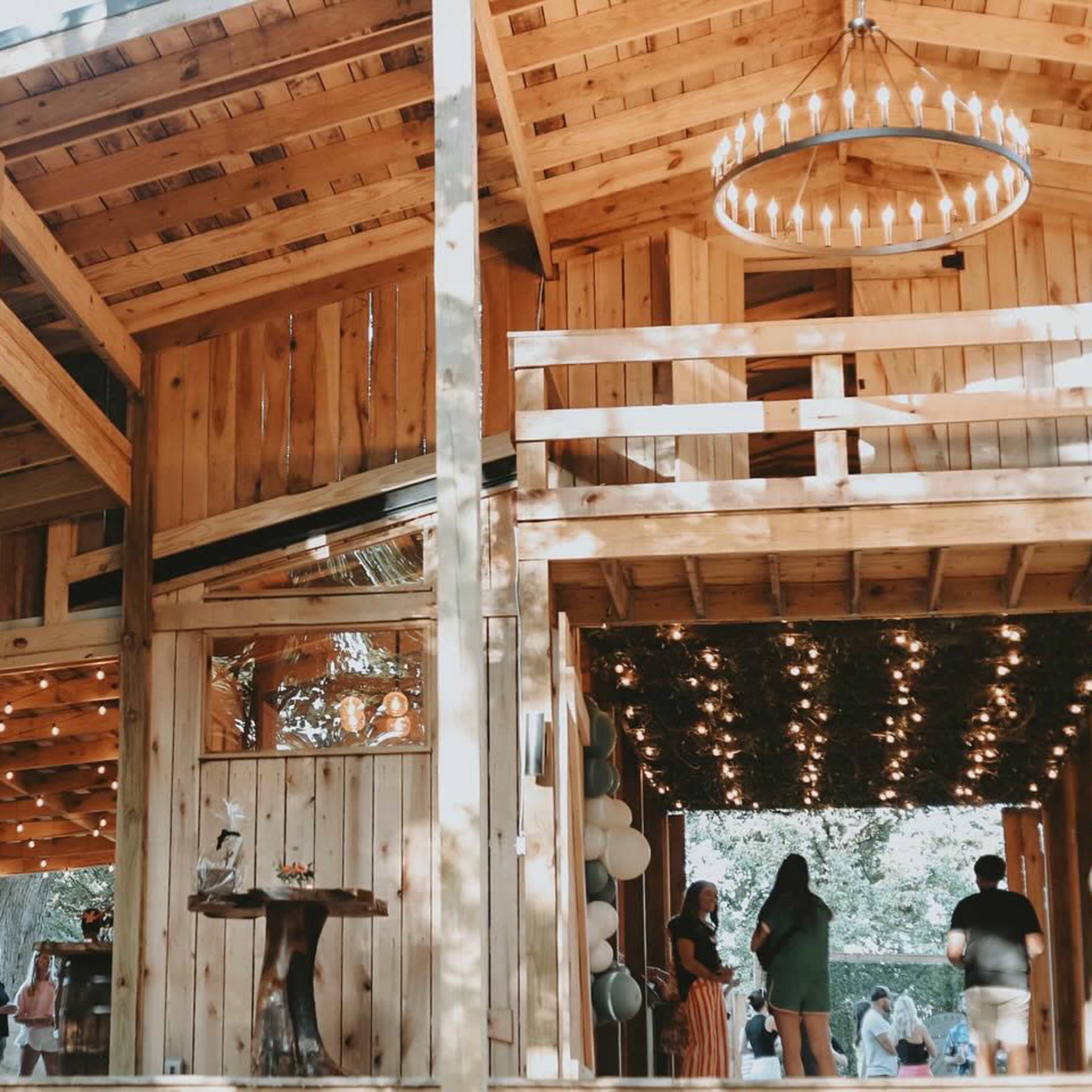 A wooden structure features an outdoor patio with string lights, while people gather inside and outside the building.
