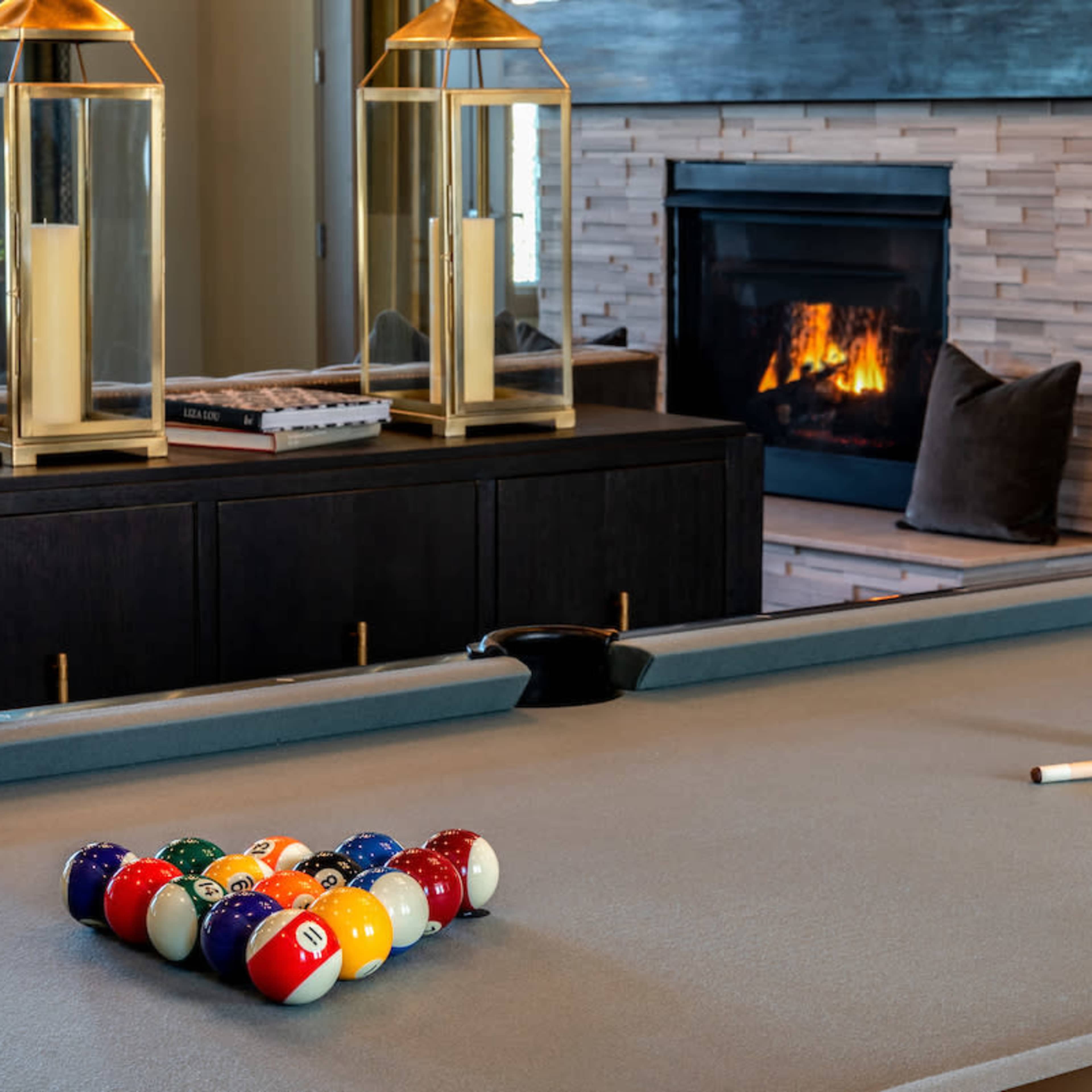 A pool table with a set of billiard balls racked up is positioned in front of a modern fireplace.