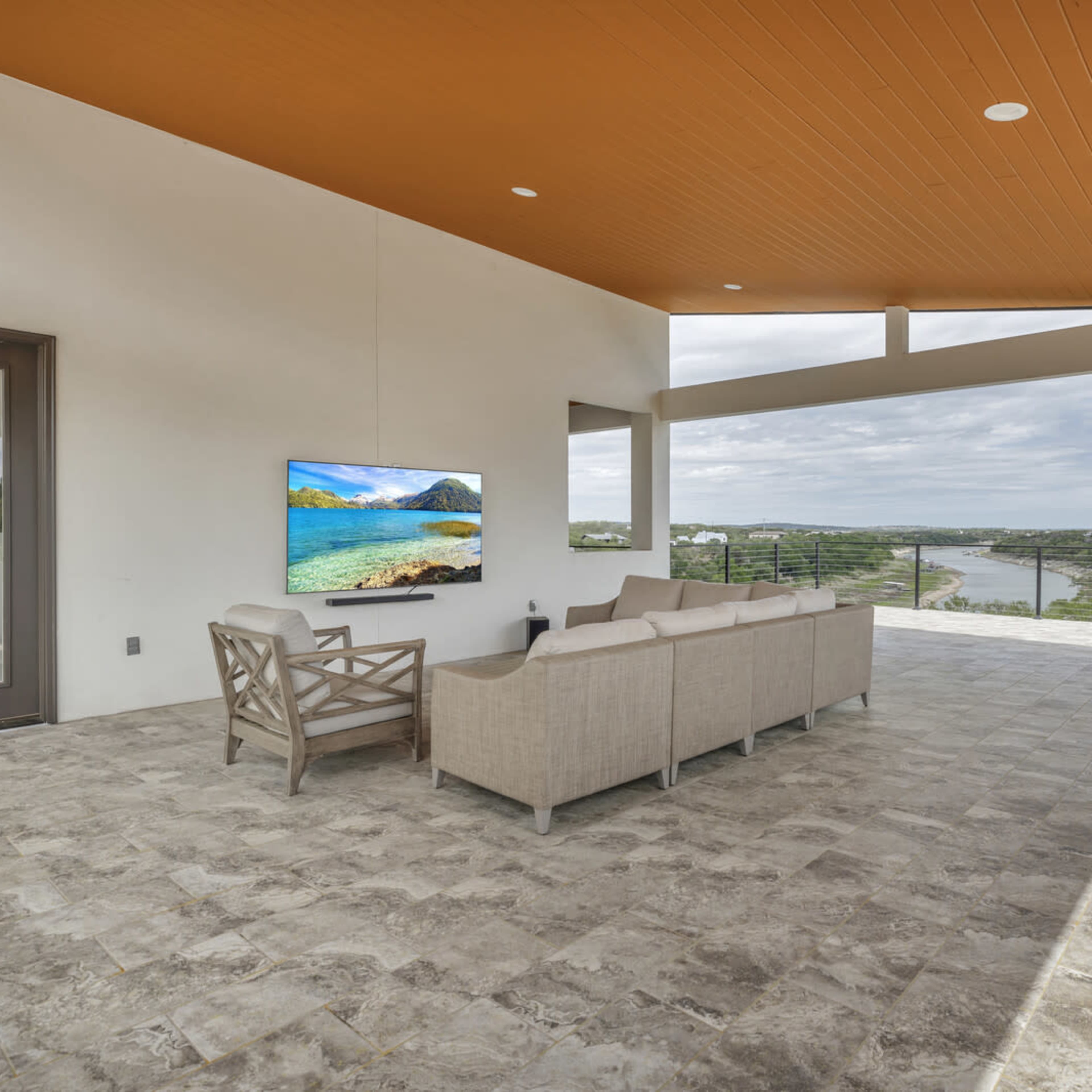 A modern outdoor living space with a sectional sofa and a wall-mounted television, overlooking a scenic landscape with a winding river.