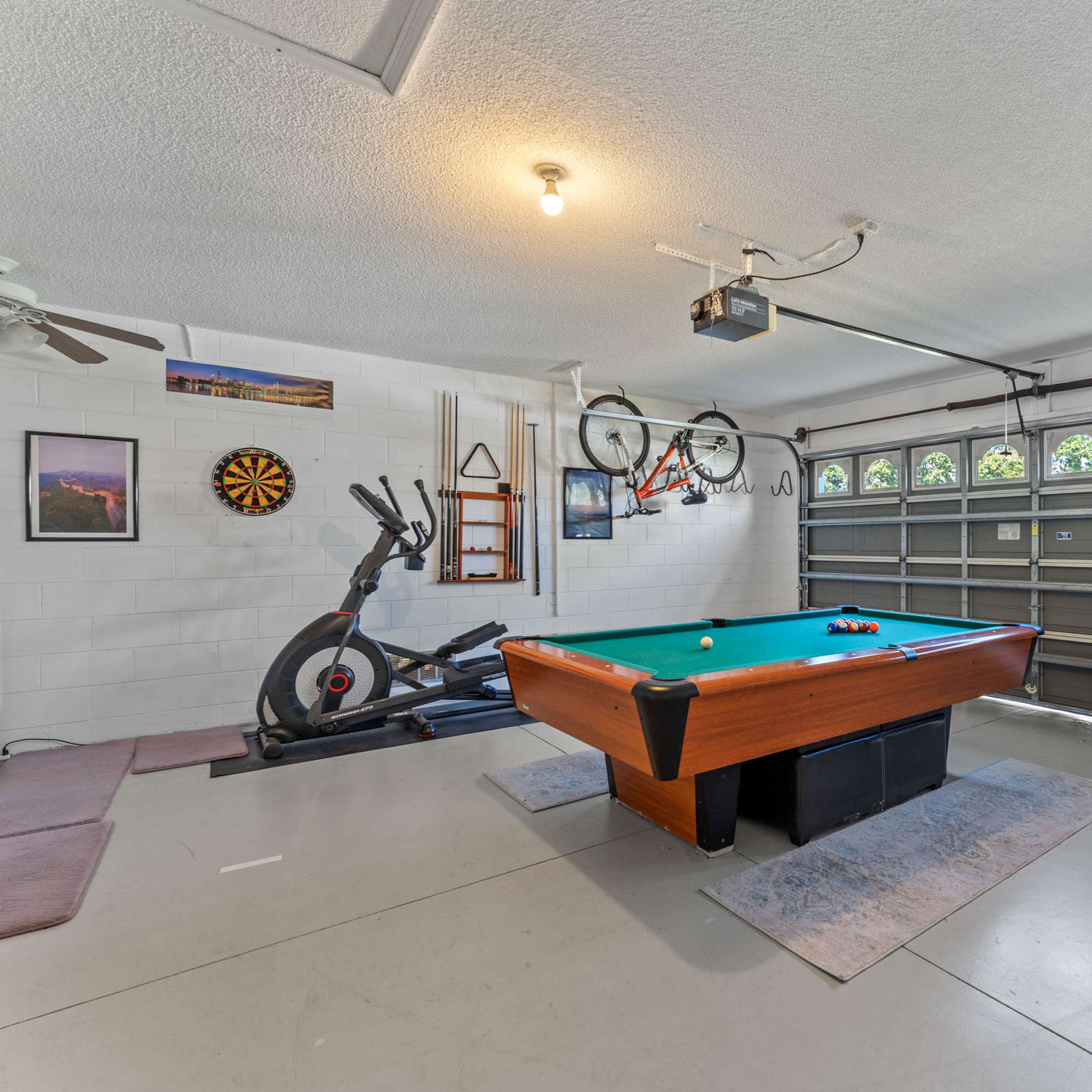 A garage with a pool table, an exercise bike, and a door with multiple windows.