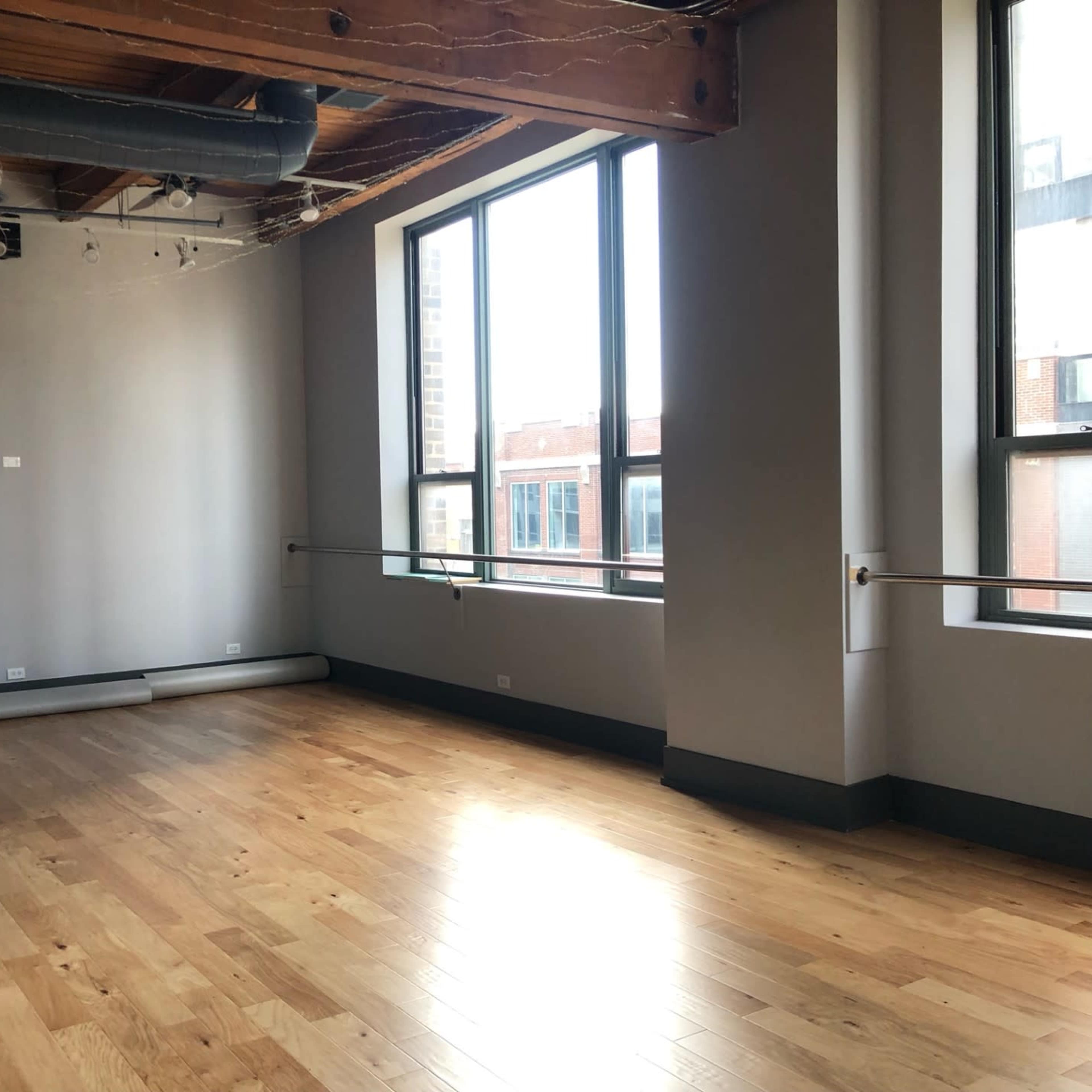 An empty room with large windows, wooden floors, and exposed beam ceilings.