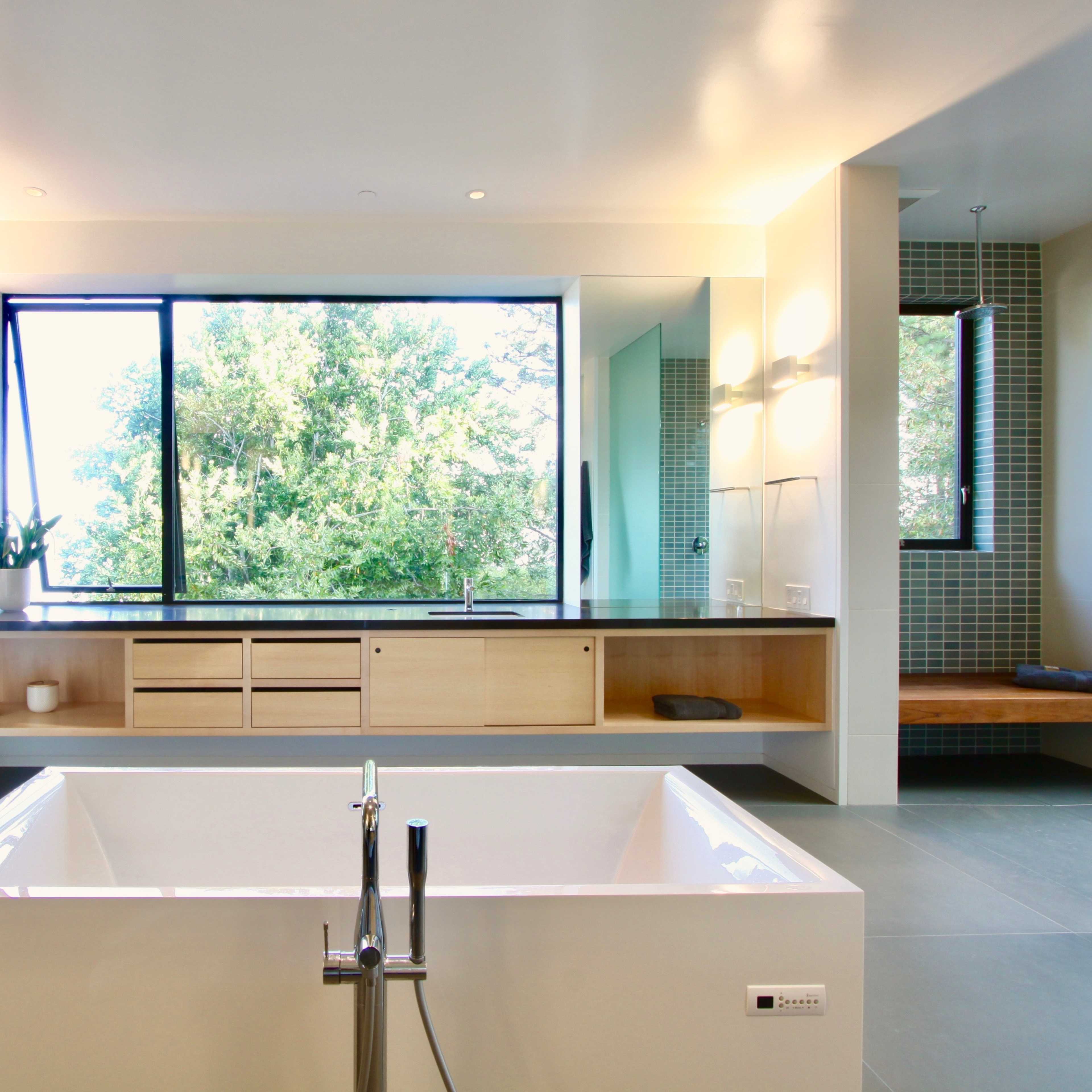 The bathroom features a freestanding bathtub in front of a large window overlooking greenery, with a modern wooden cabinet and wall panels.