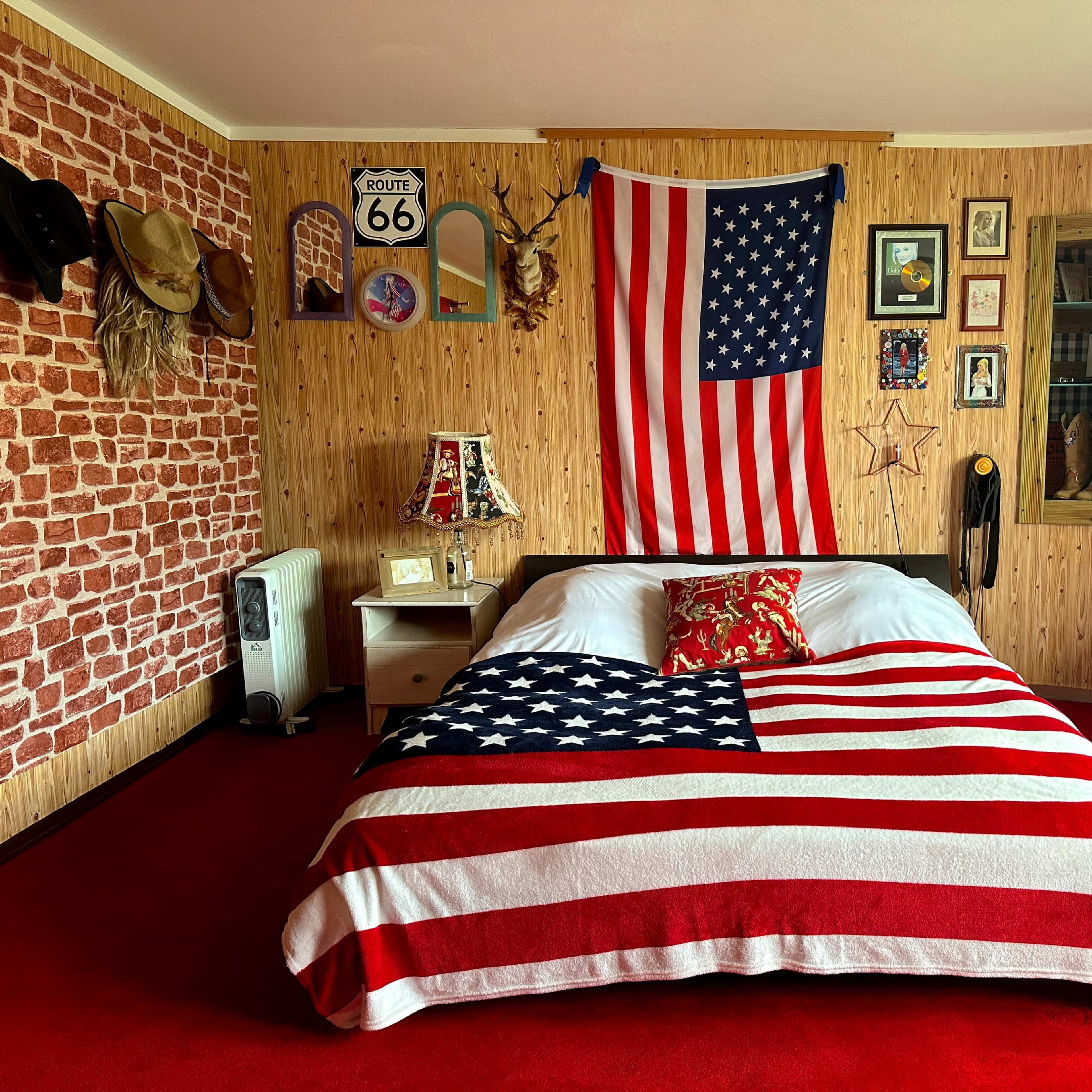 The room features a bed covered with an American flag blanket, surrounded by red carpet and decorated with various wall hangings and memorabilia.