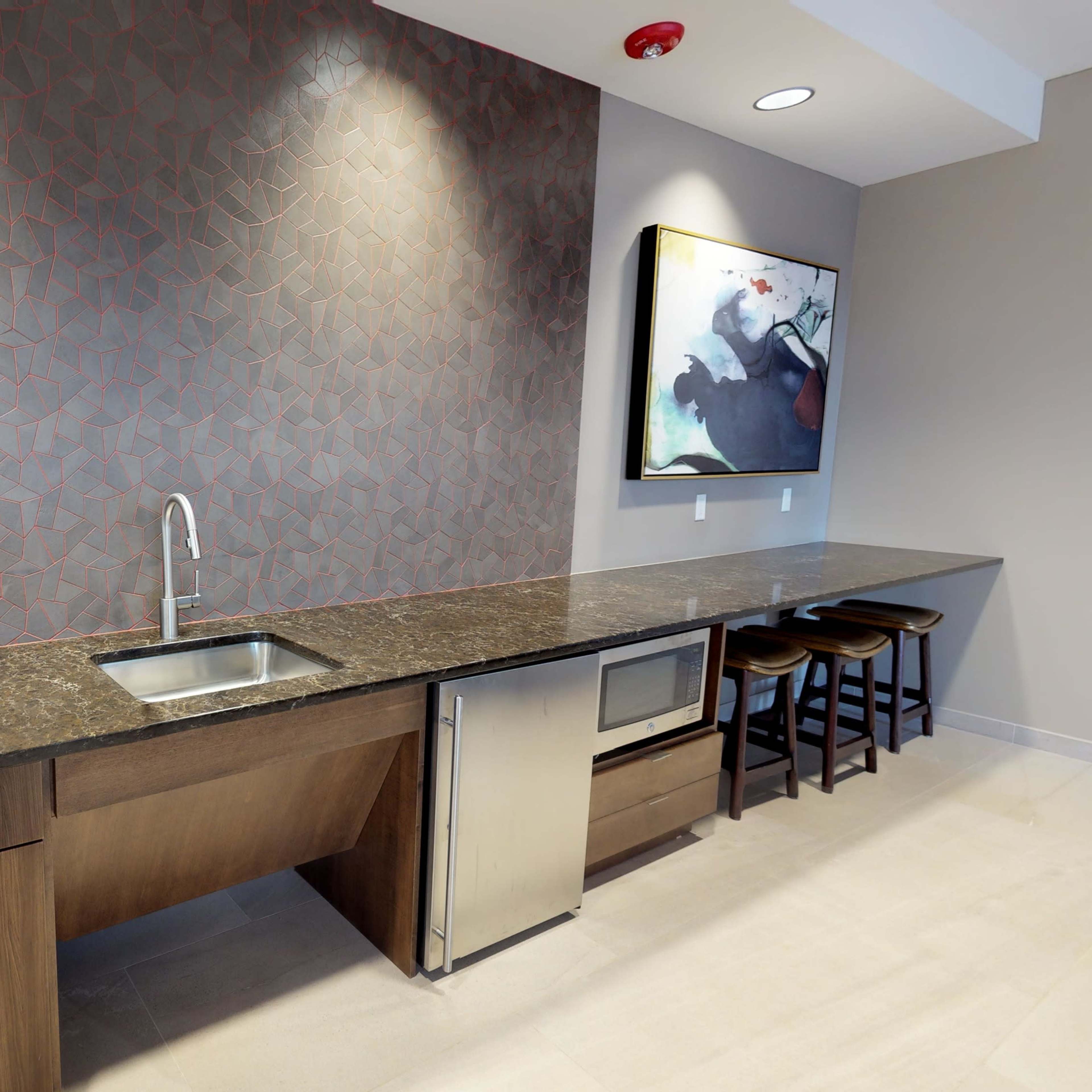 A modern kitchen features a dark countertop, a stainless steel sink, and a refrigerator, against a patterned wall with framed artwork above.