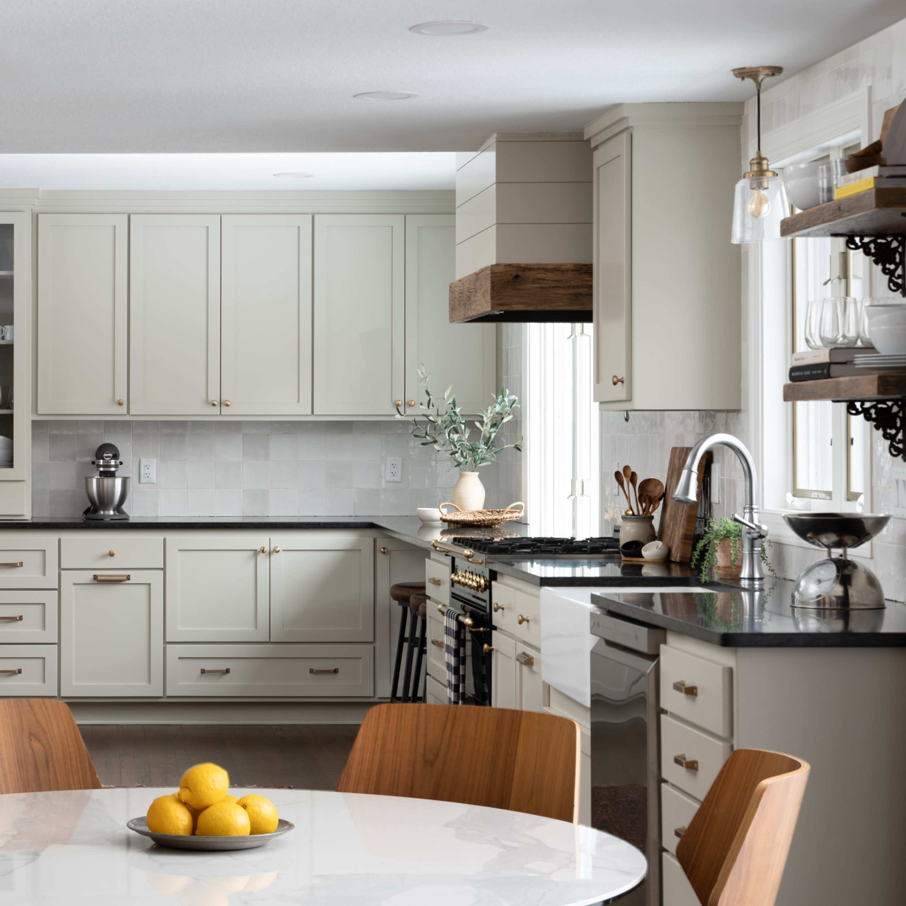 A modern kitchen features light-colored cabinetry, a round dining table with a centerpiece of lemons, and a stainless steel refrigerator.