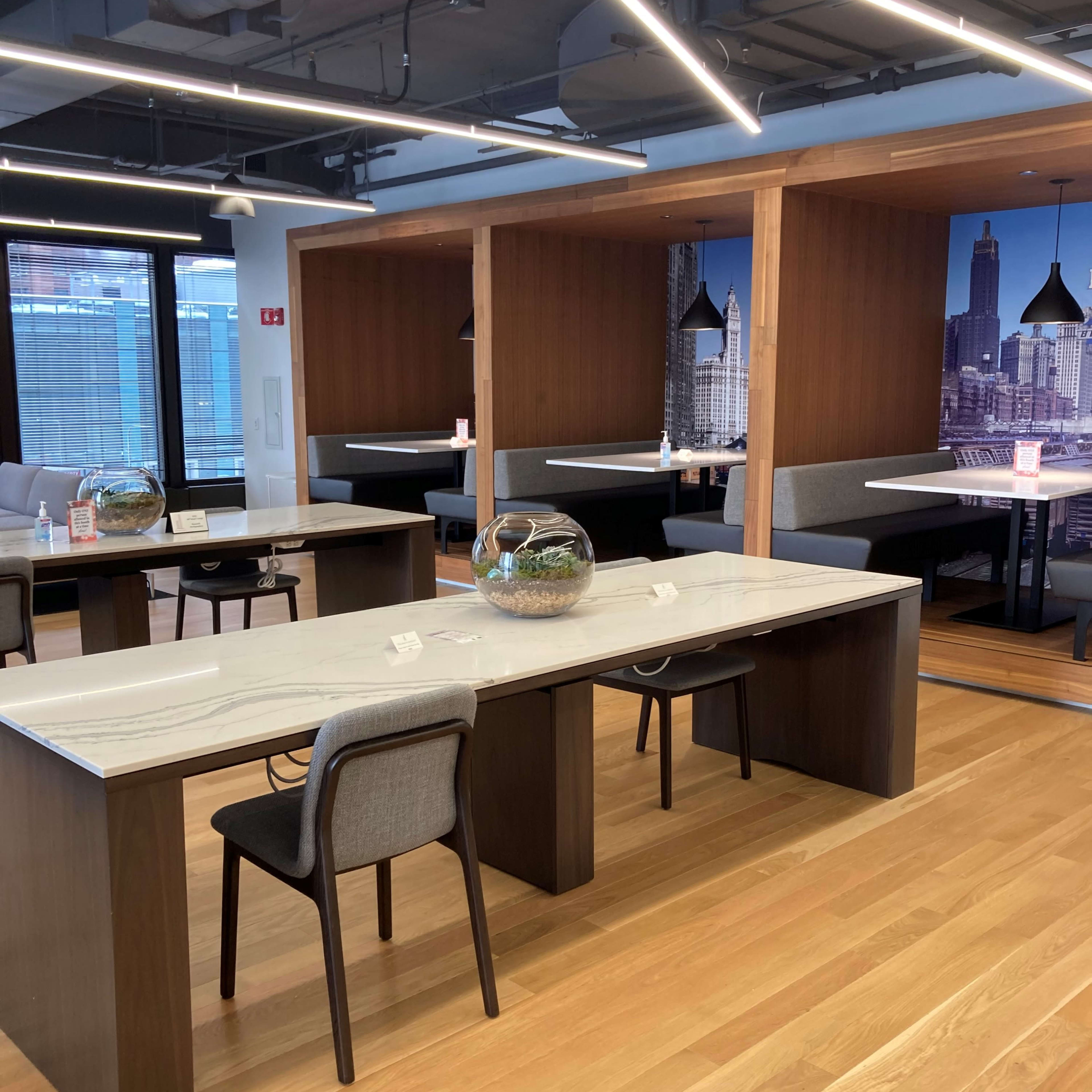 A modern dining area with sleek wooden tables, gray chairs, and private booths decorated with a city skyline mural.