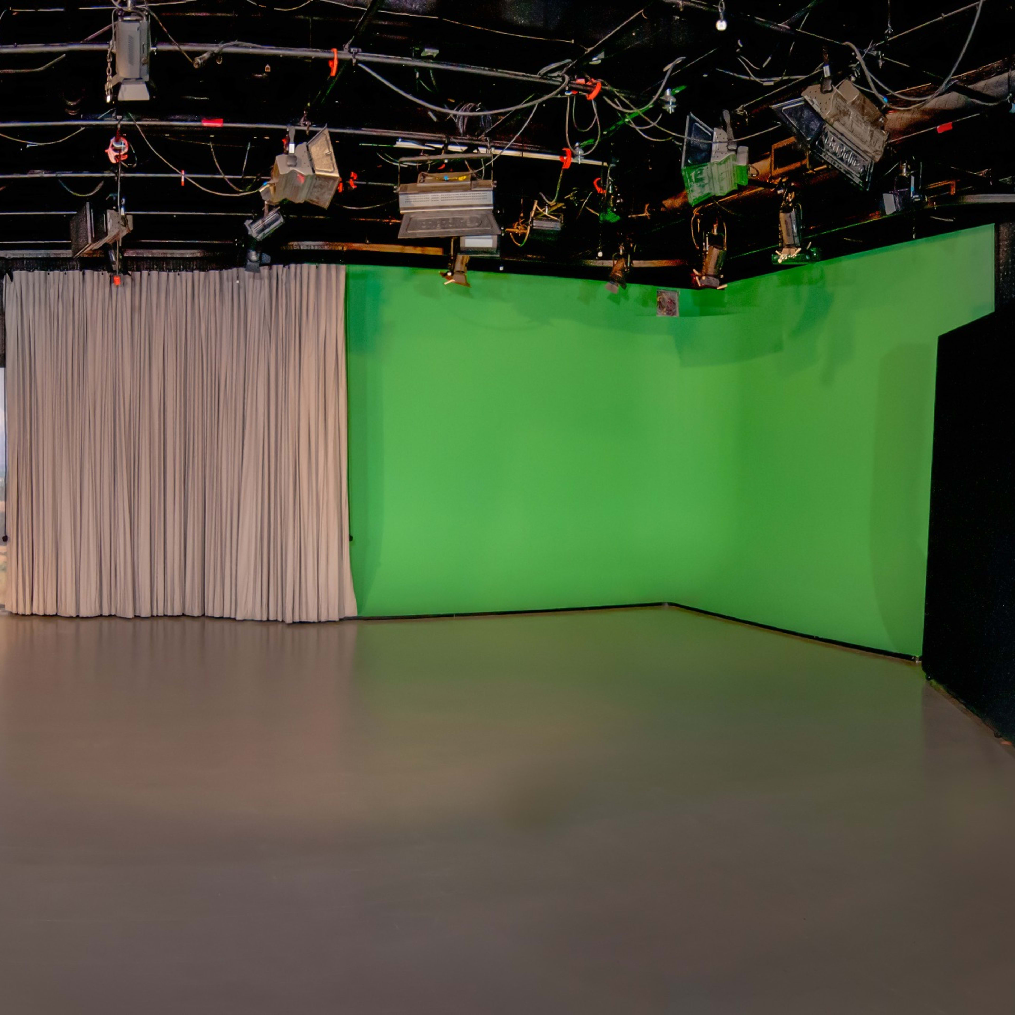A panoramic view of a television studio with a green screen wall, a black desk, and curtains in a simple layout.