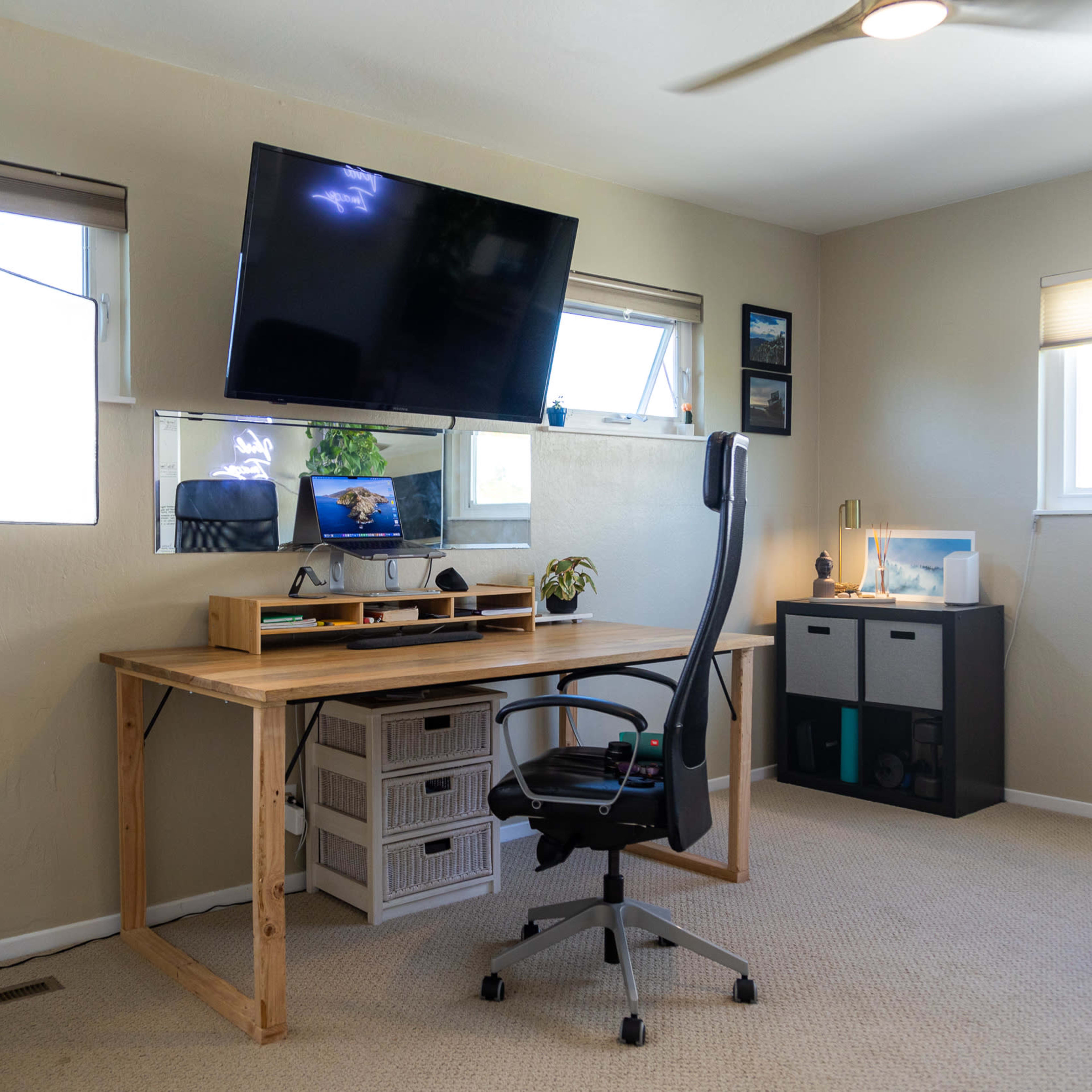 A minimalist home office setup featuring a wooden desk, an ergonomic chair, a wall-mounted television, and a studio light stand.