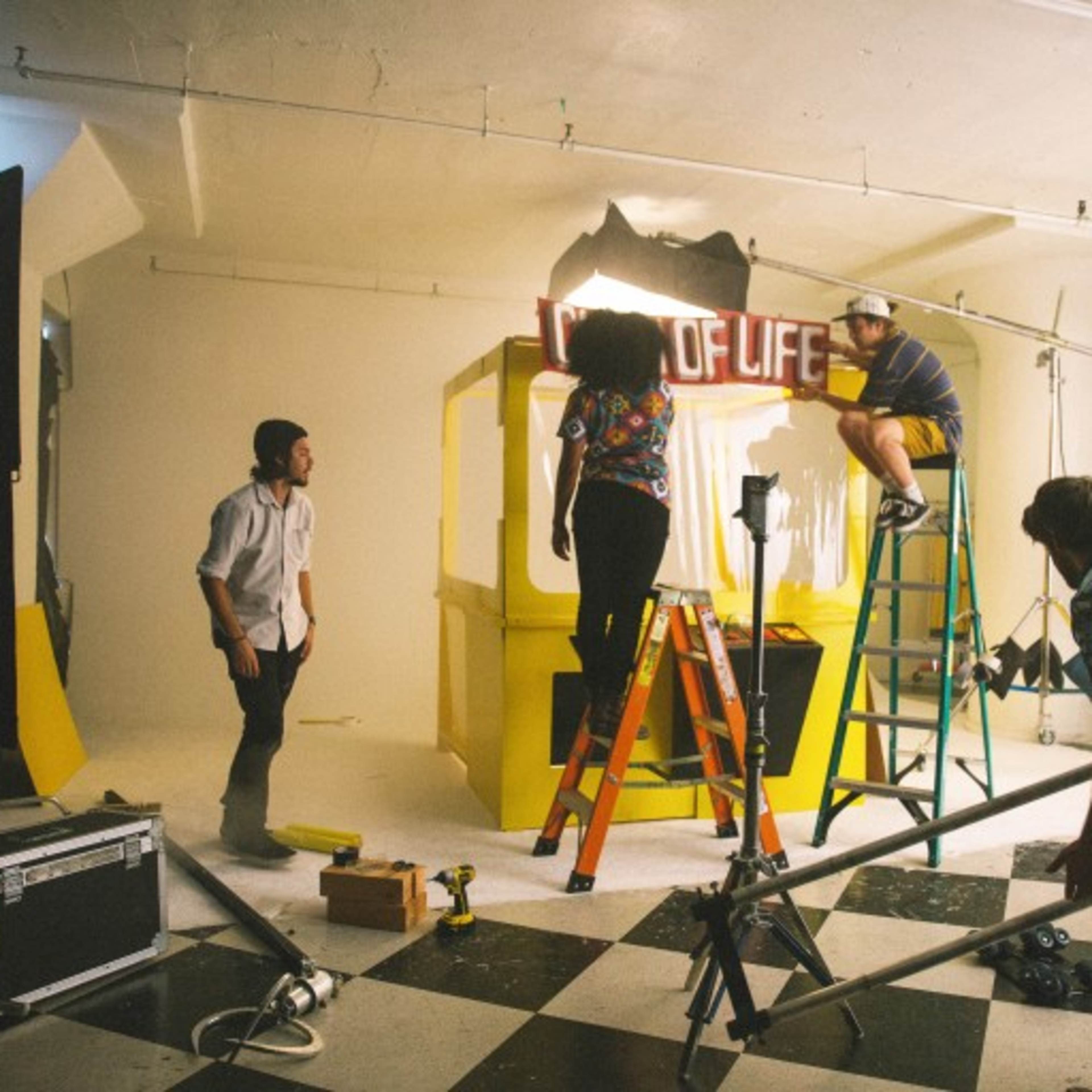 A group of four people set up a colorful display in a studio, with ladders and equipment scattered around.